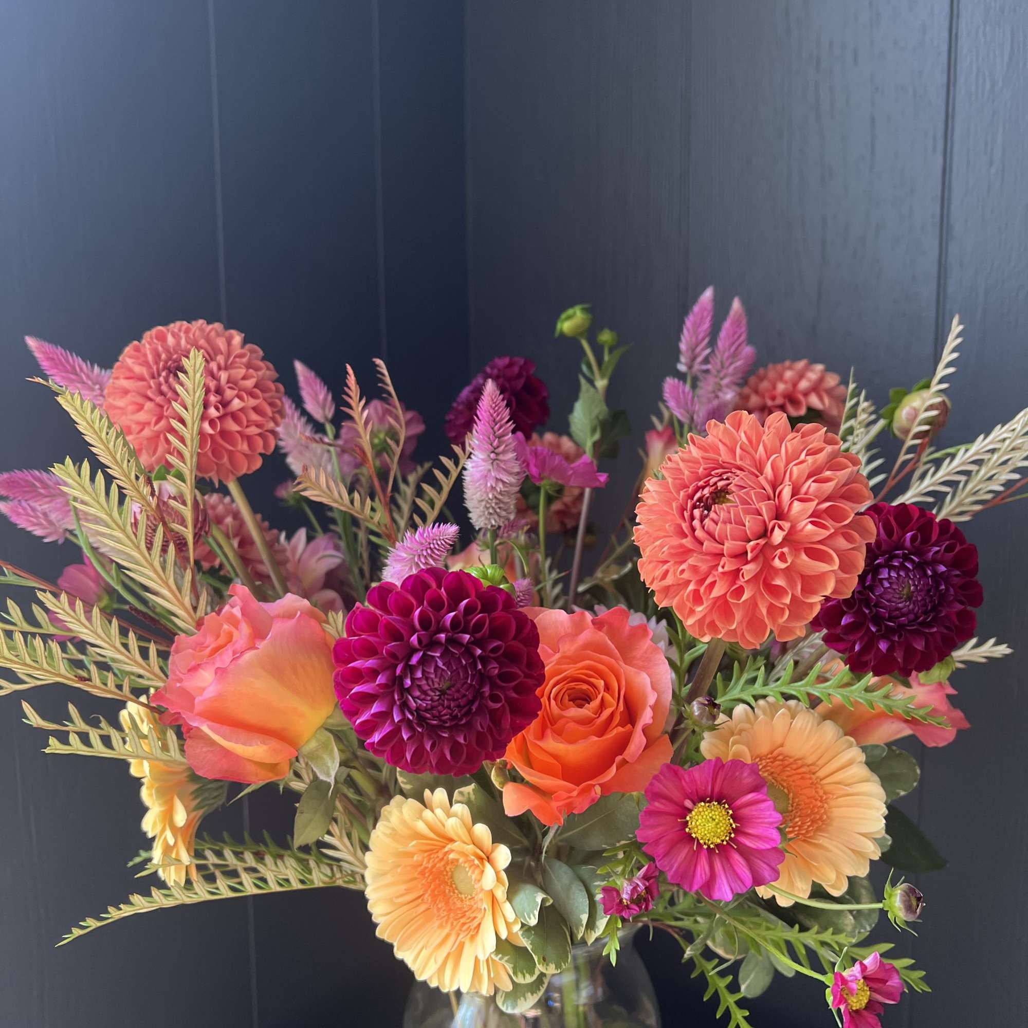 Bright mixed bouquet of dahlias, roses, and gerbera daisies in a glass vase