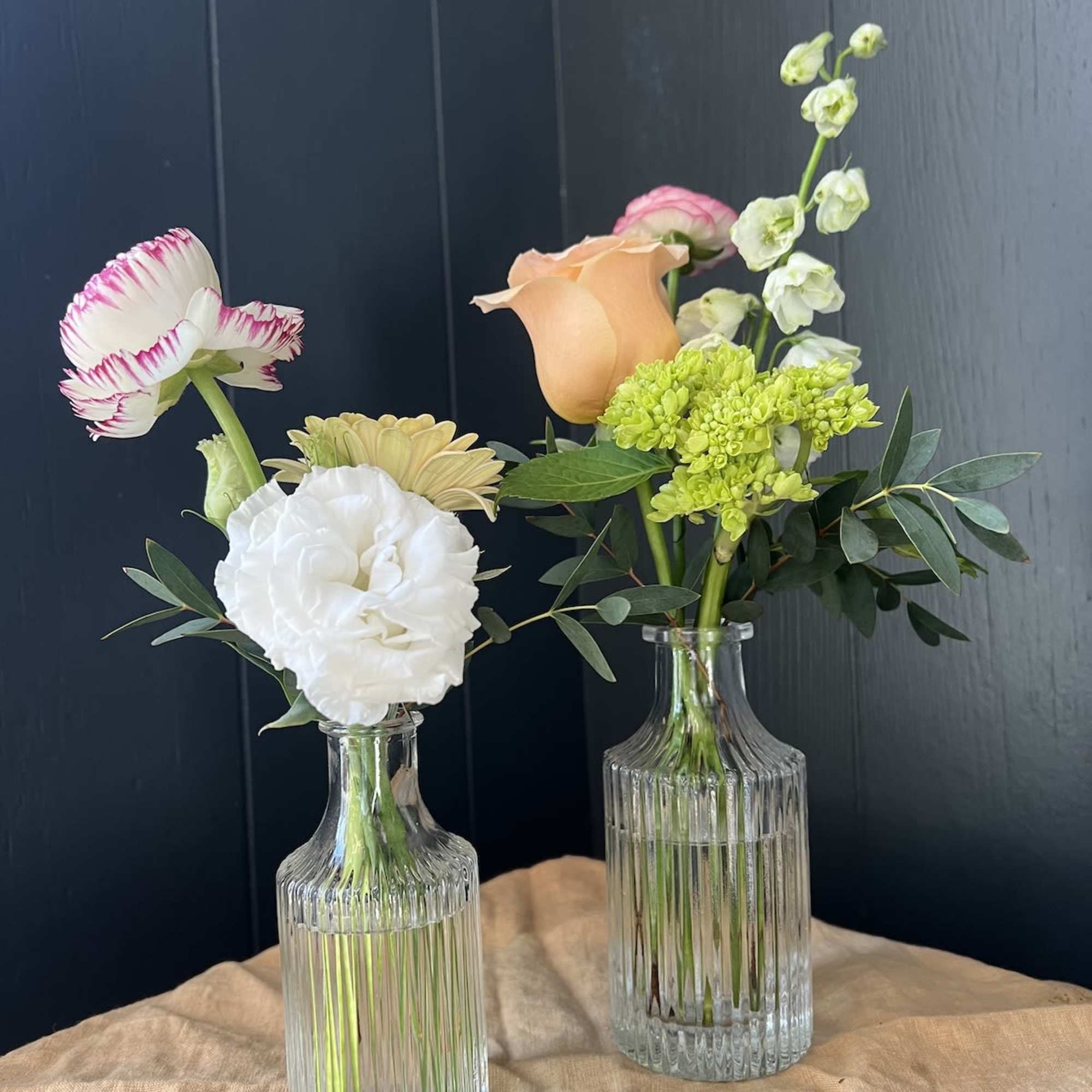 Two small floral arrangements in clear glass bottles with mixed blooms.