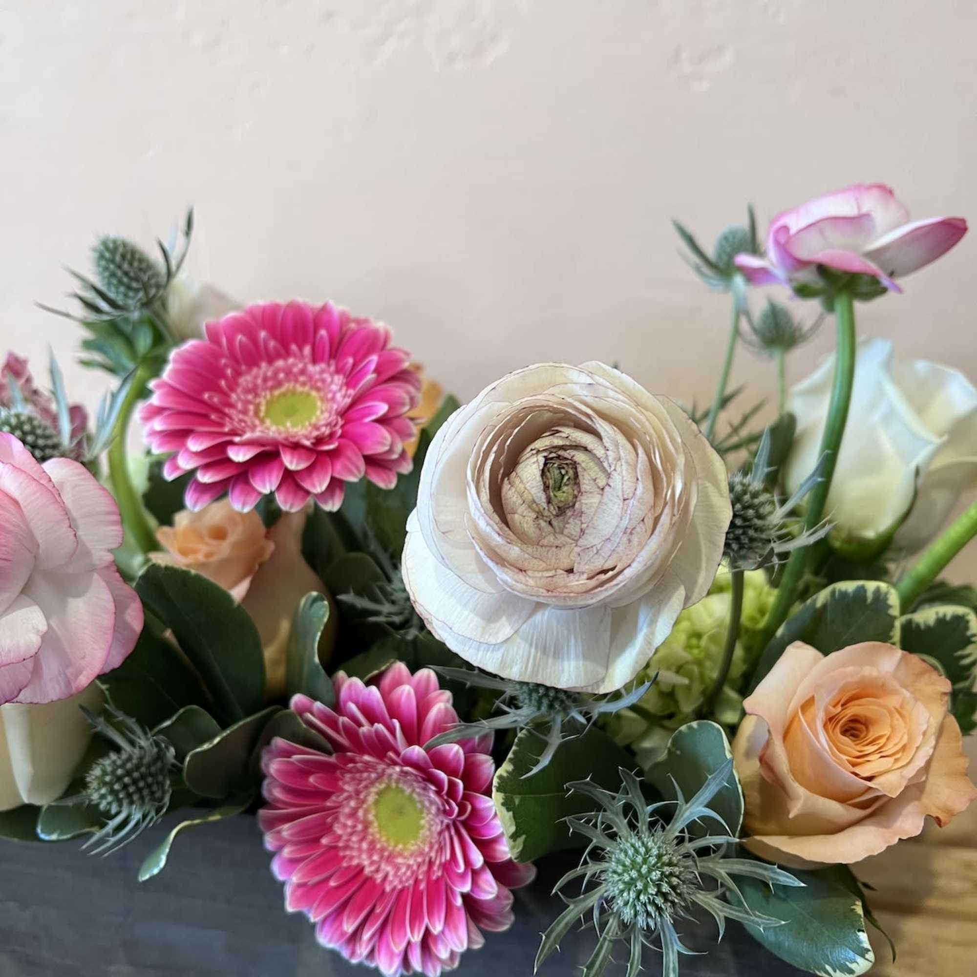 Mixed bouquet with pink gerbera daisies, cream ranunculus, and peach roses
