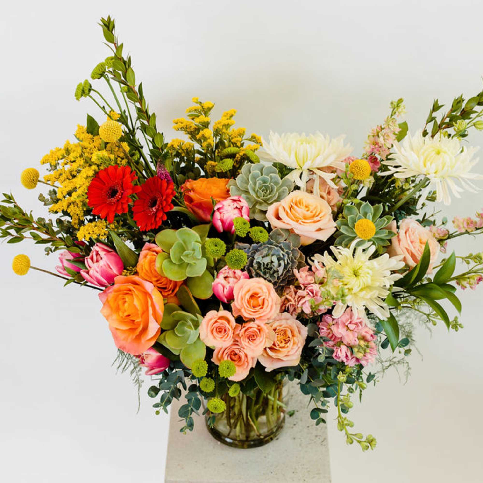 Mixed bouquet of roses, gerbera daisies, and succulents in a glass vase