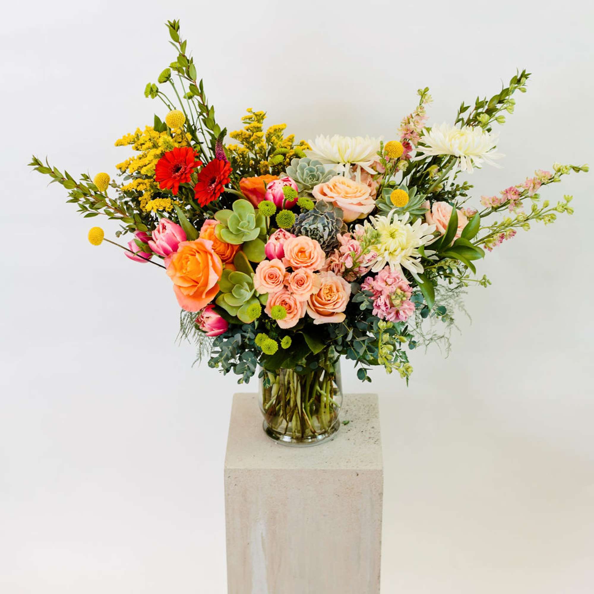 Mixed bouquet of roses, succulents, and daisies in a glass vase