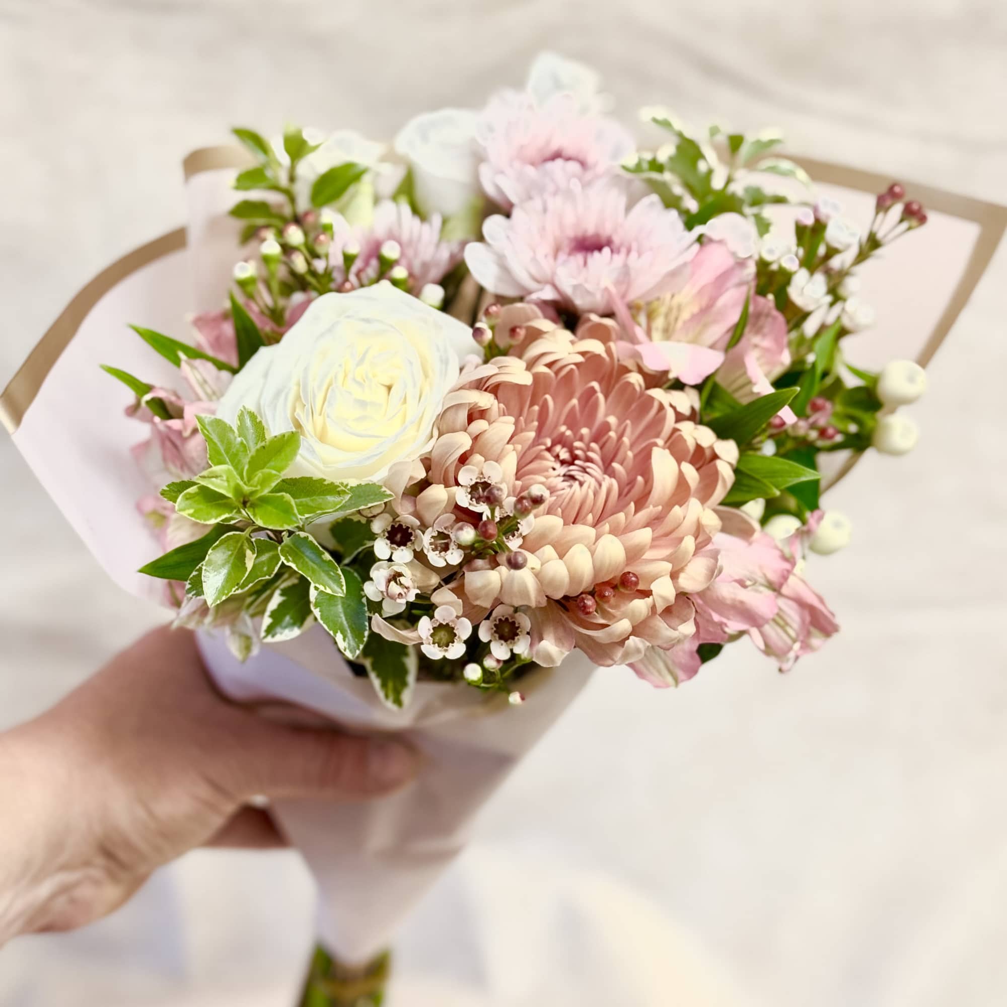 Handheld bouquet of pale pink and white flowers wrapped in paper