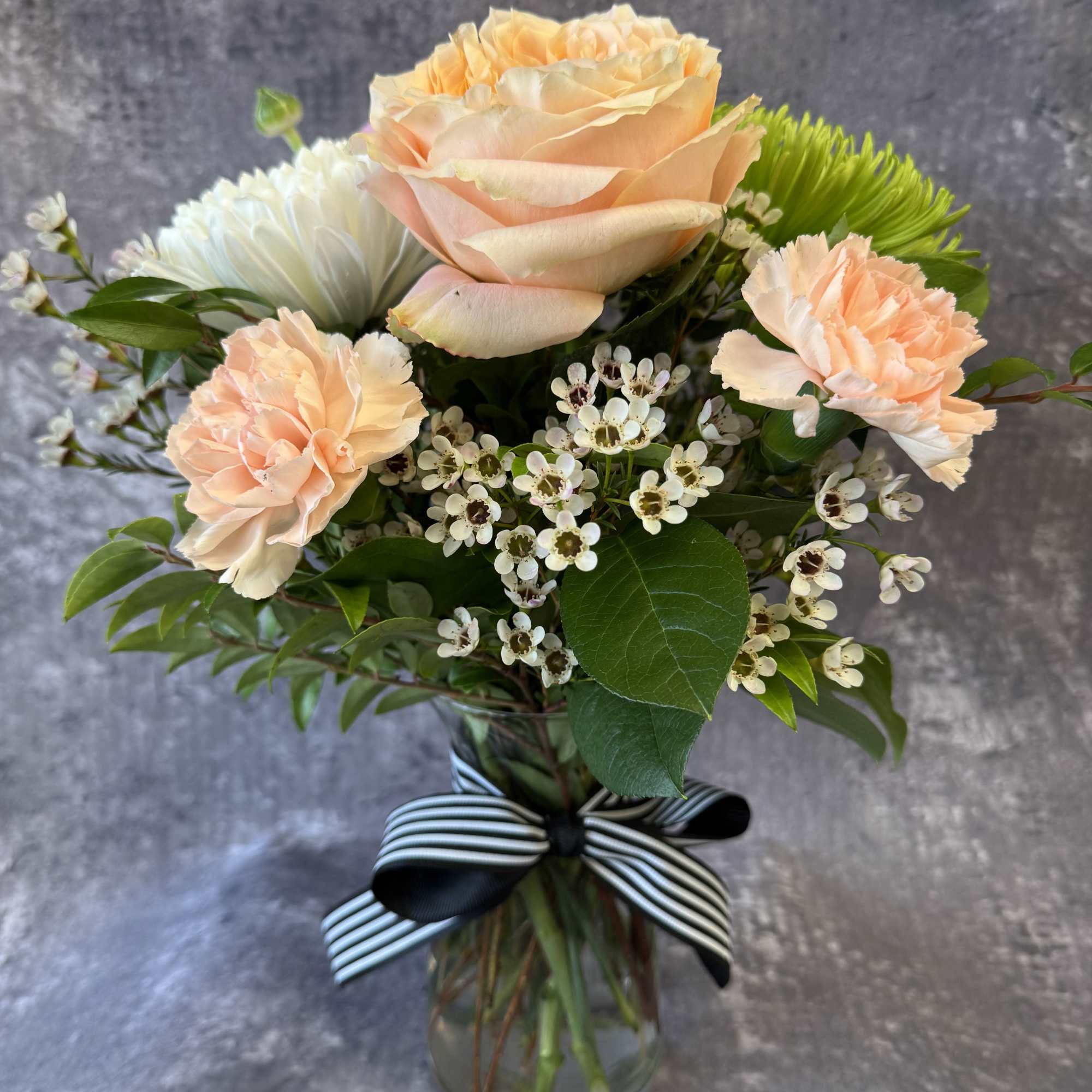 Peach roses and carnations in a glass vase with a striped ribbon