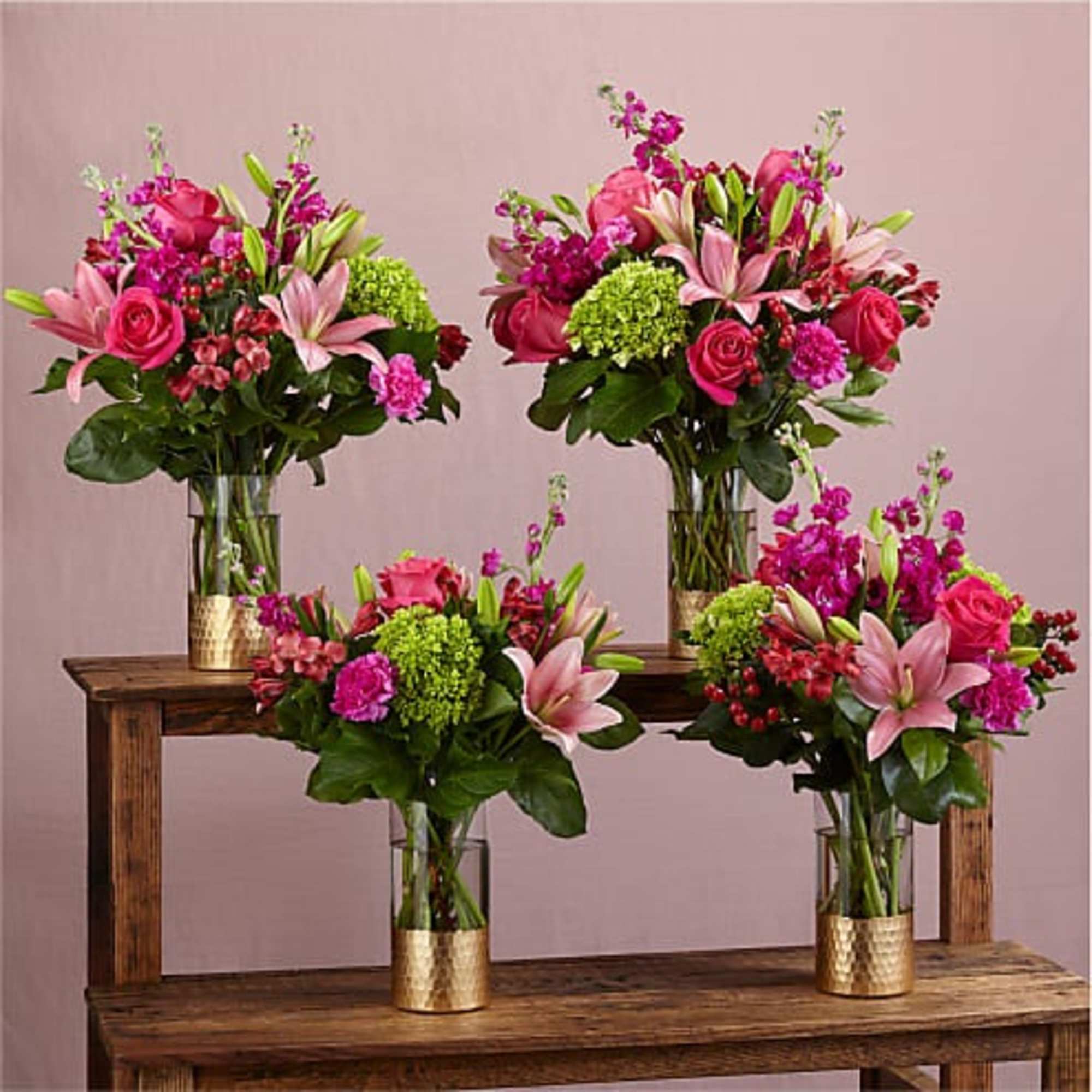 Four pink and magenta floral arrangements in gold vases on wooden stands