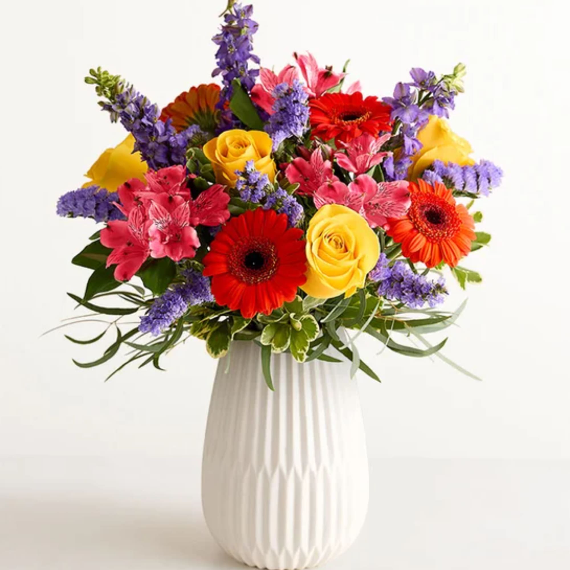 Colorful mixed bouquet in a white vase with roses and gerbera daisies