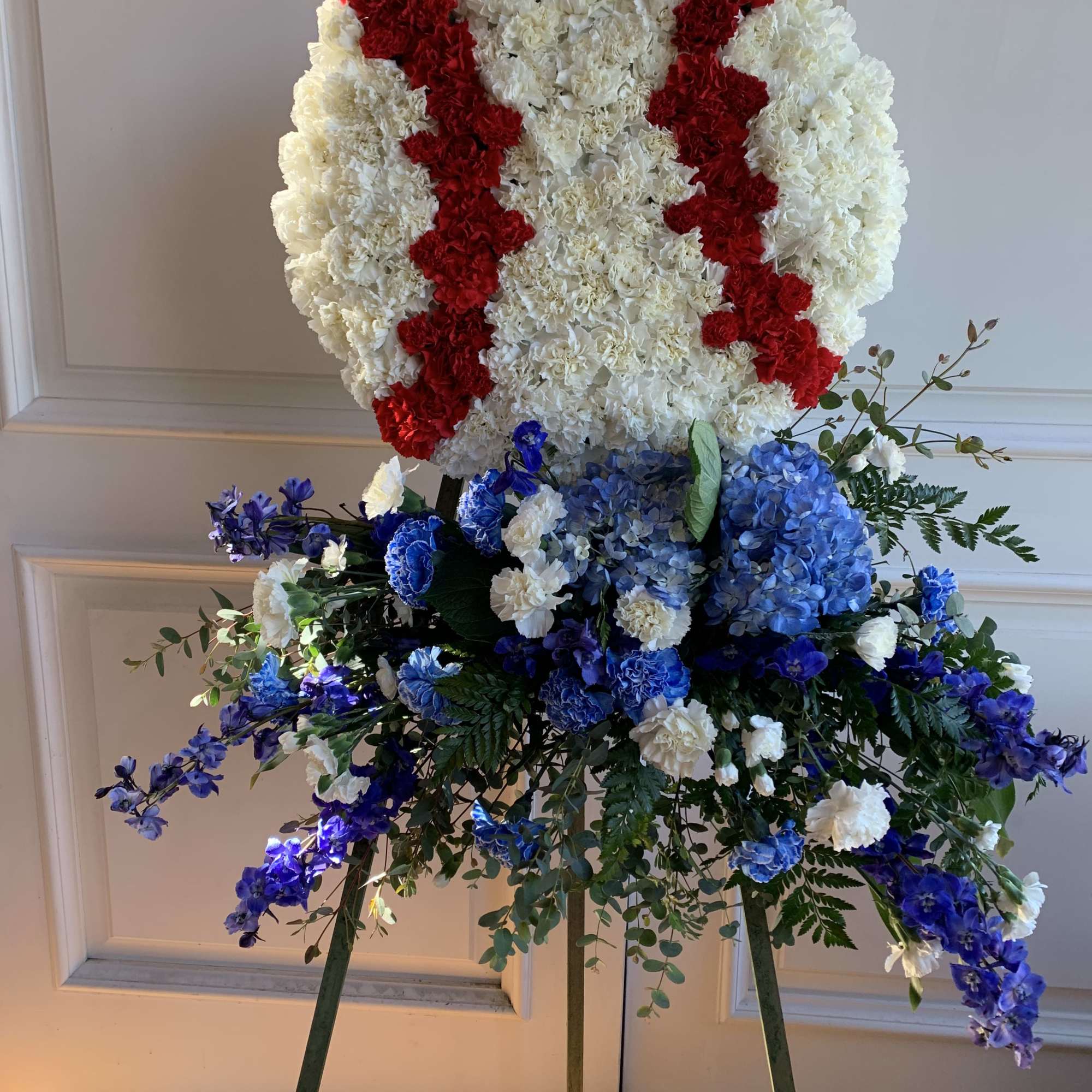 Large standing floral tribute with white, red, and blue flowers on an easel