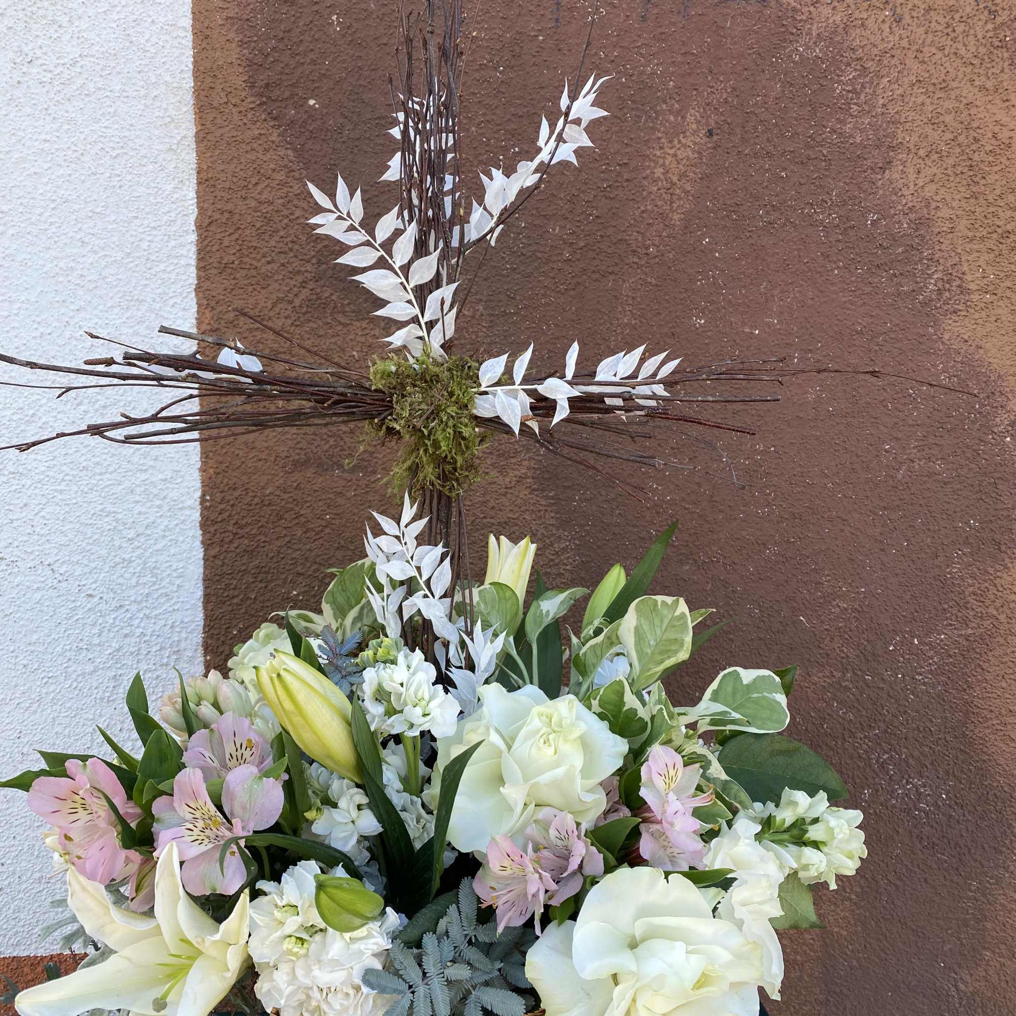 White and pale pink floral arrangement in a wicker basket with a tall cross centerpiece