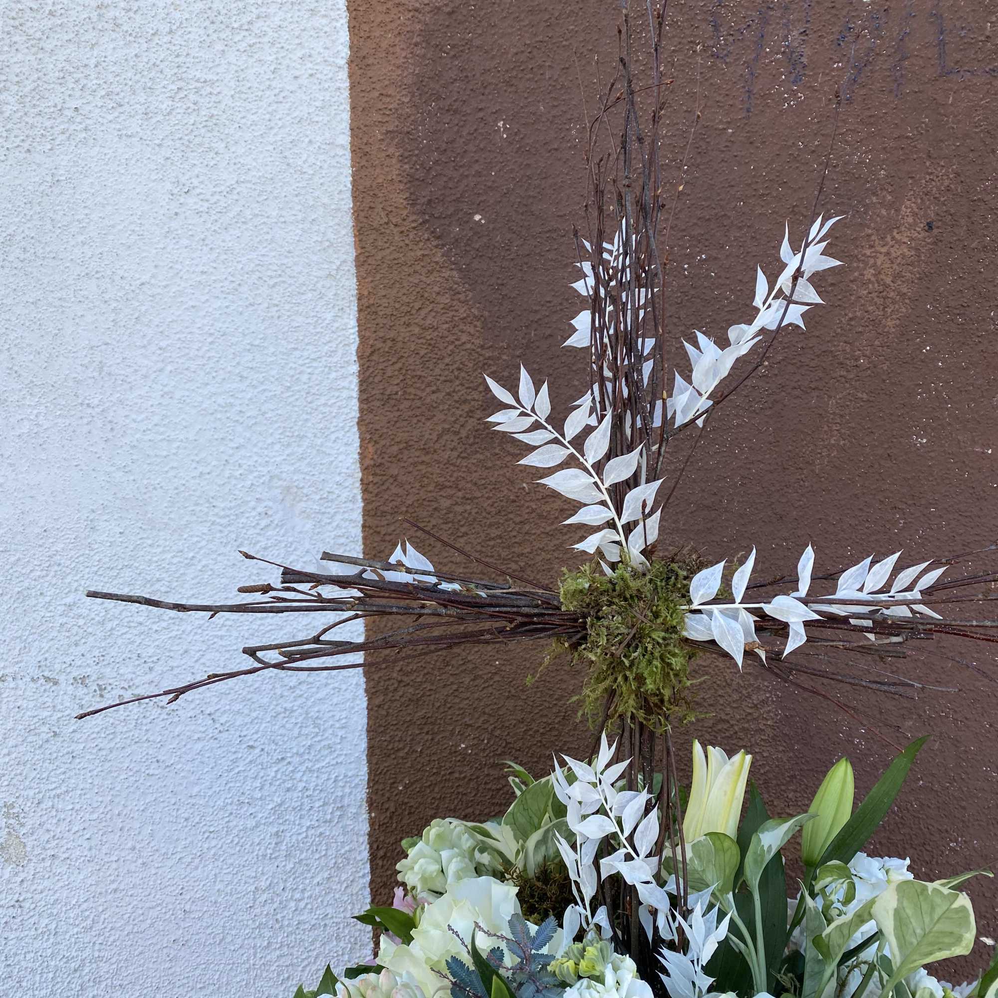 Tall floral arrangement with white lilies and roses beneath a twig cross