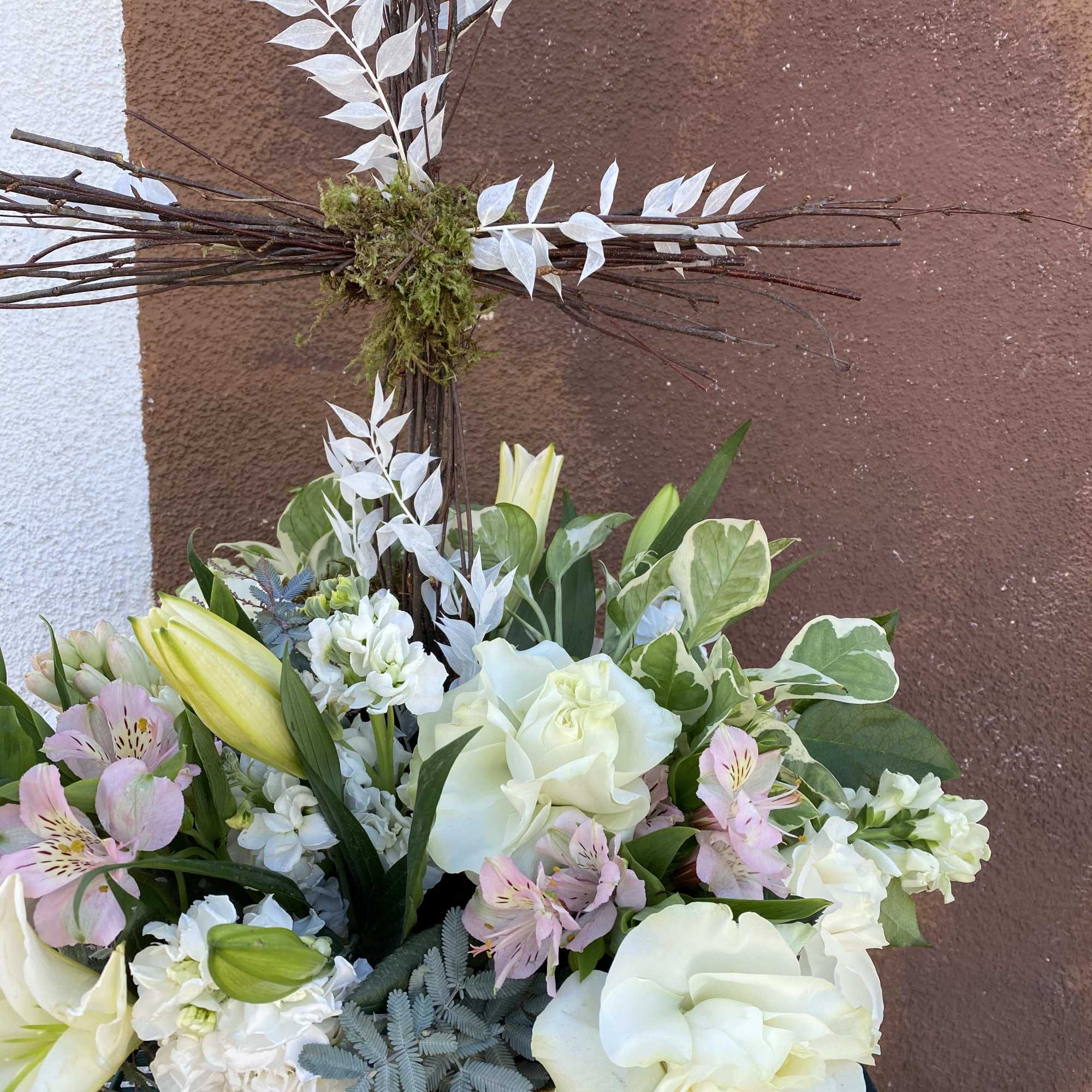 White floral arrangement in a wicker basket with a tall twig cross
