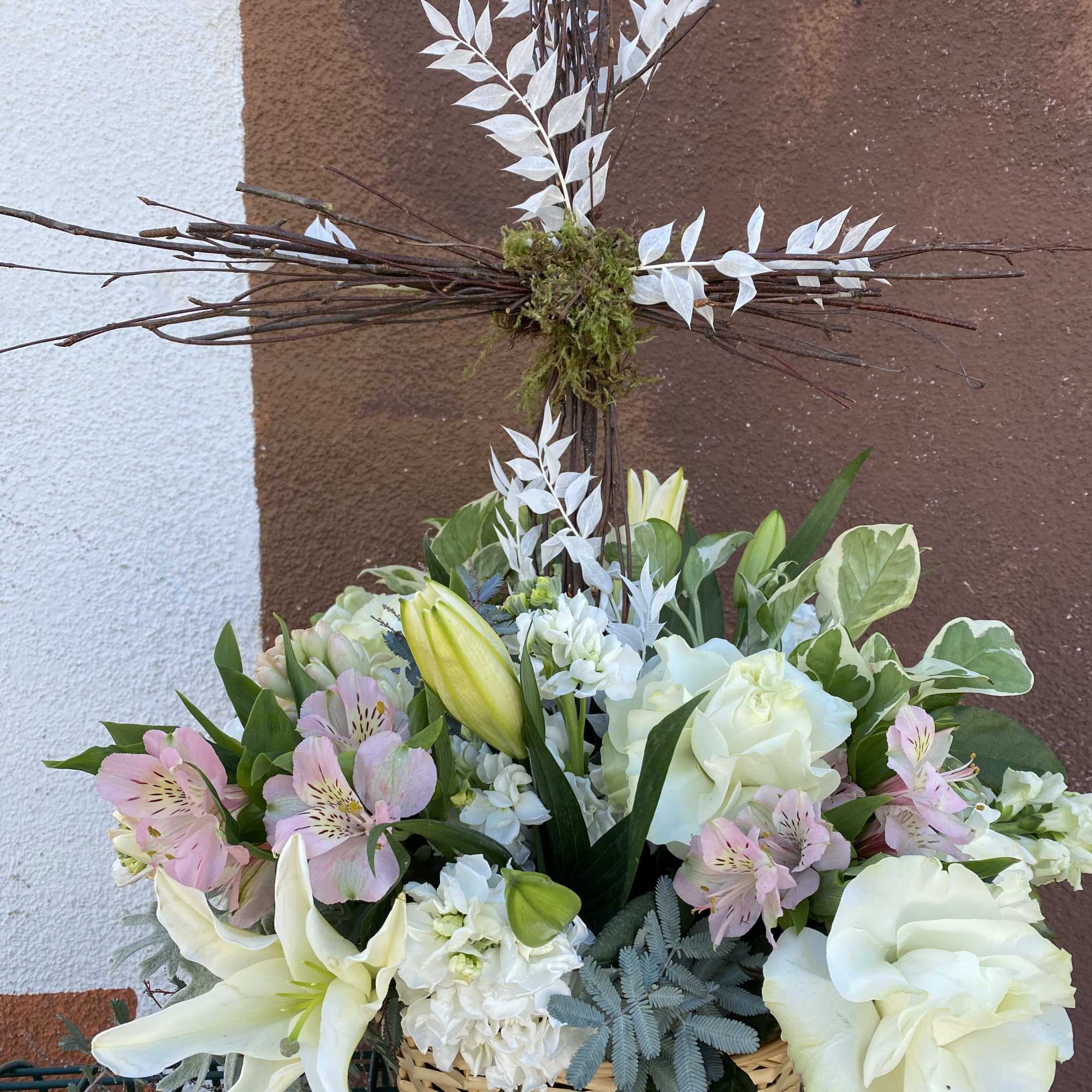 Basket arrangement of white lilies, roses, and pink flowers with a twig cross