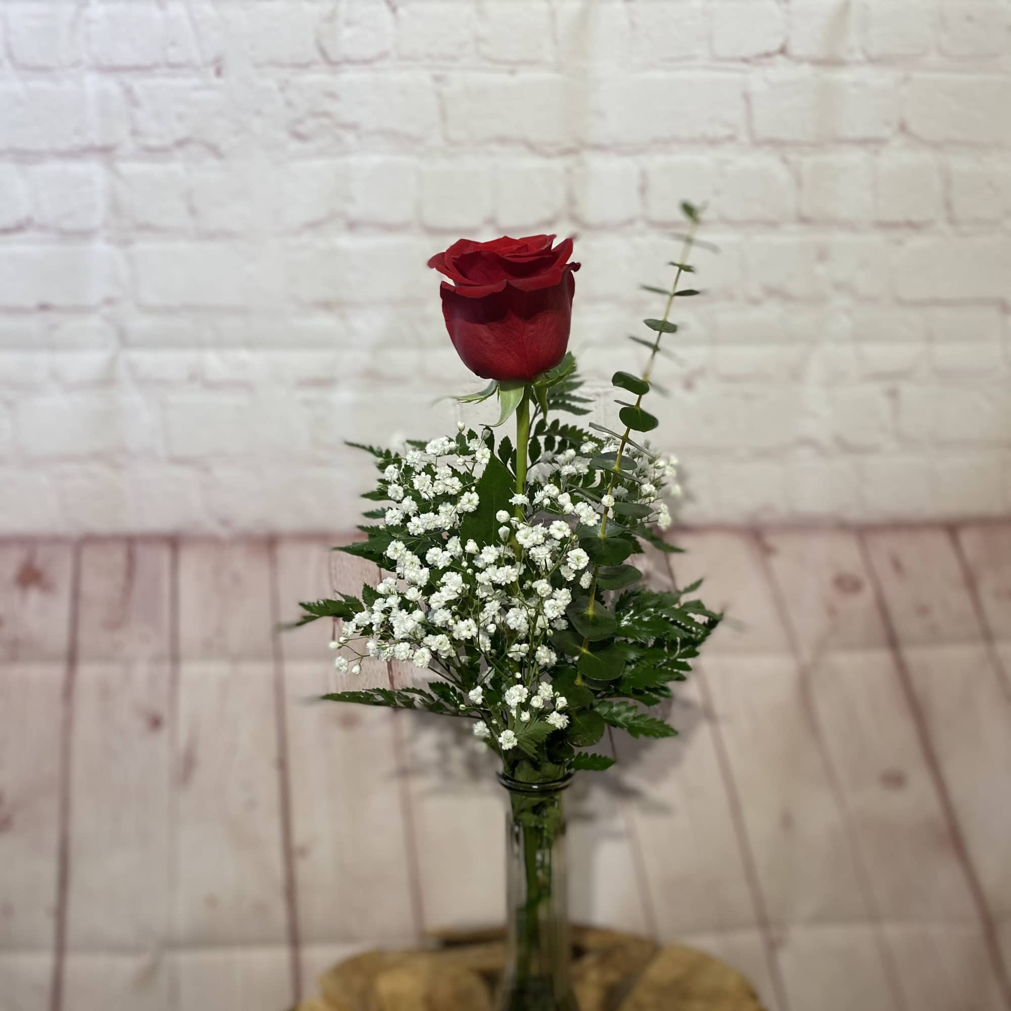 Single red rose in a clear glass vase with white filler flowers