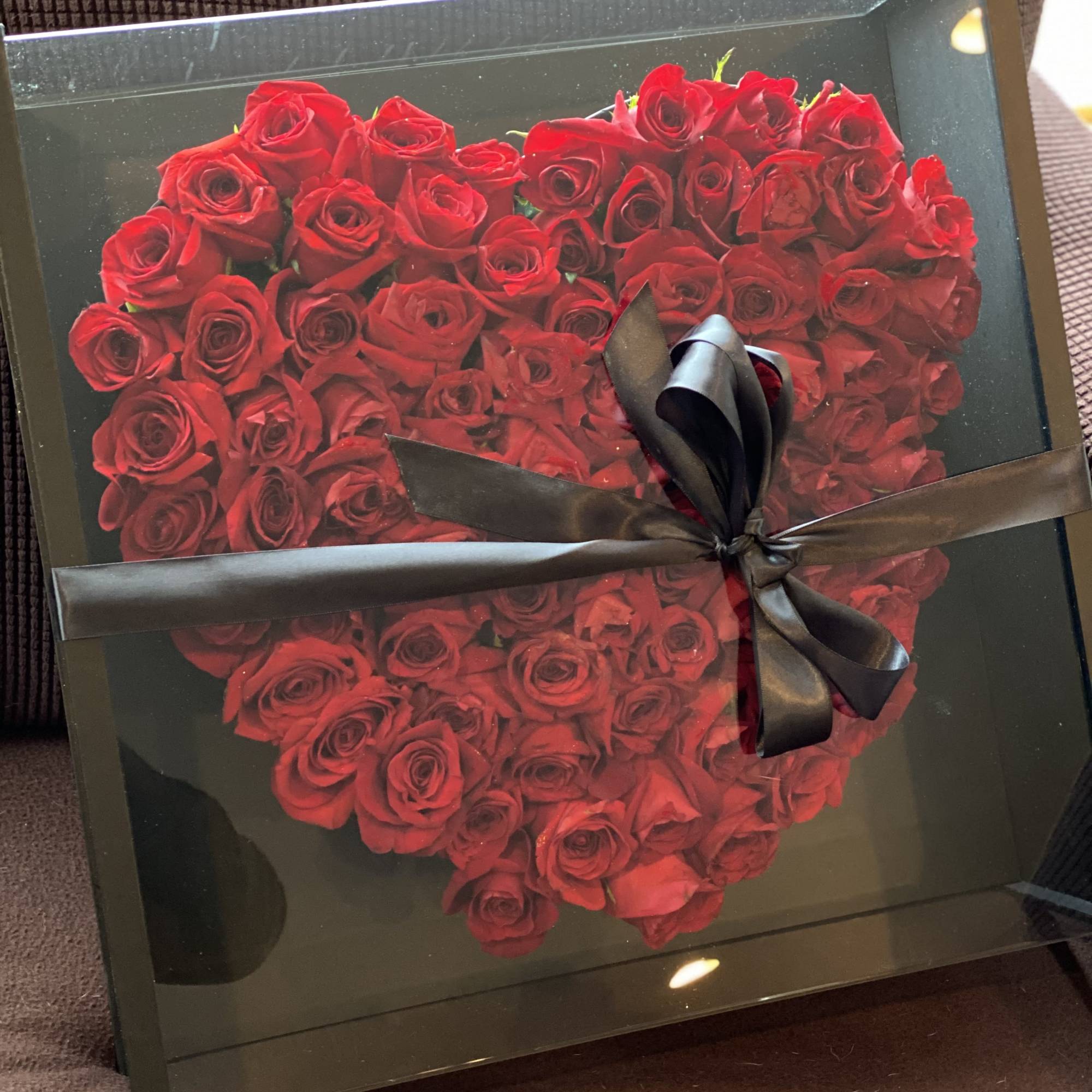 Heart-shaped box filled with red roses and tied with a black ribbon