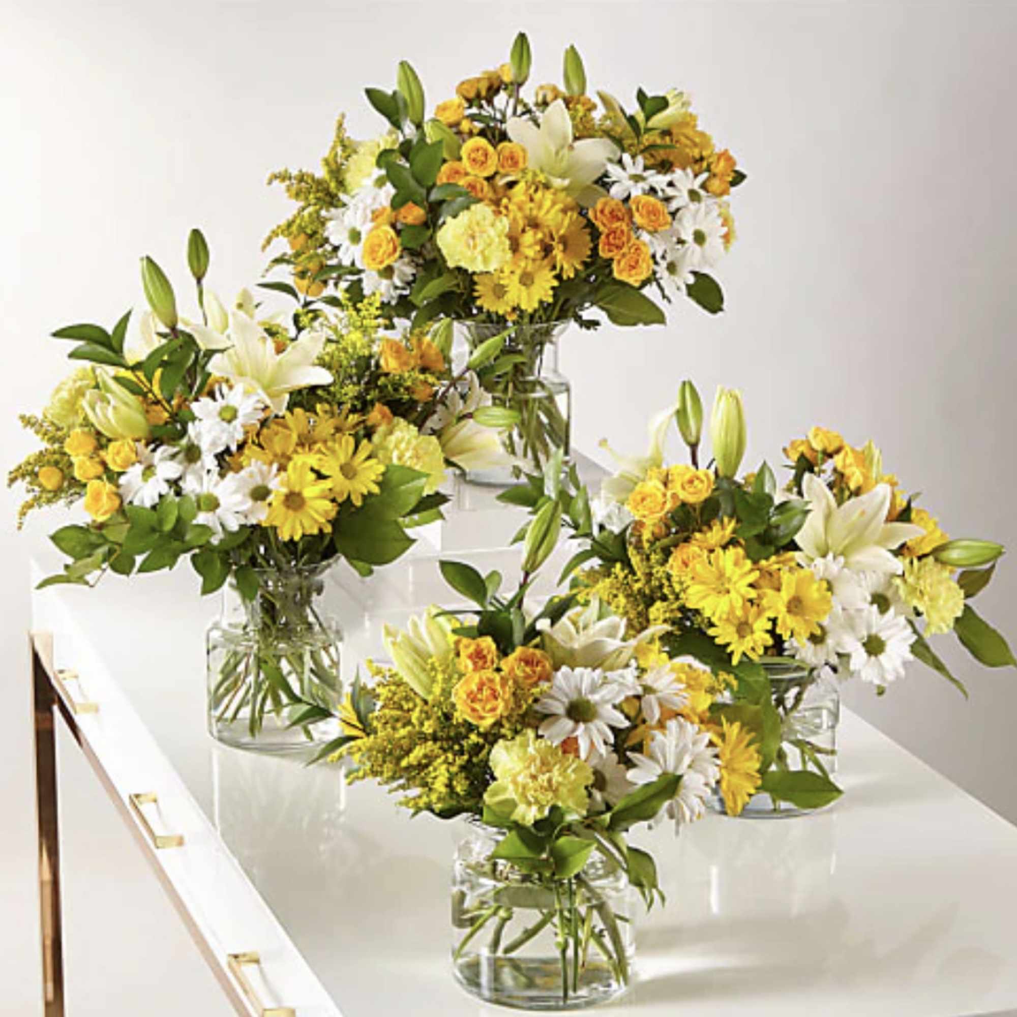 Yellow and white flower arrangements in clear glass vases on a white table