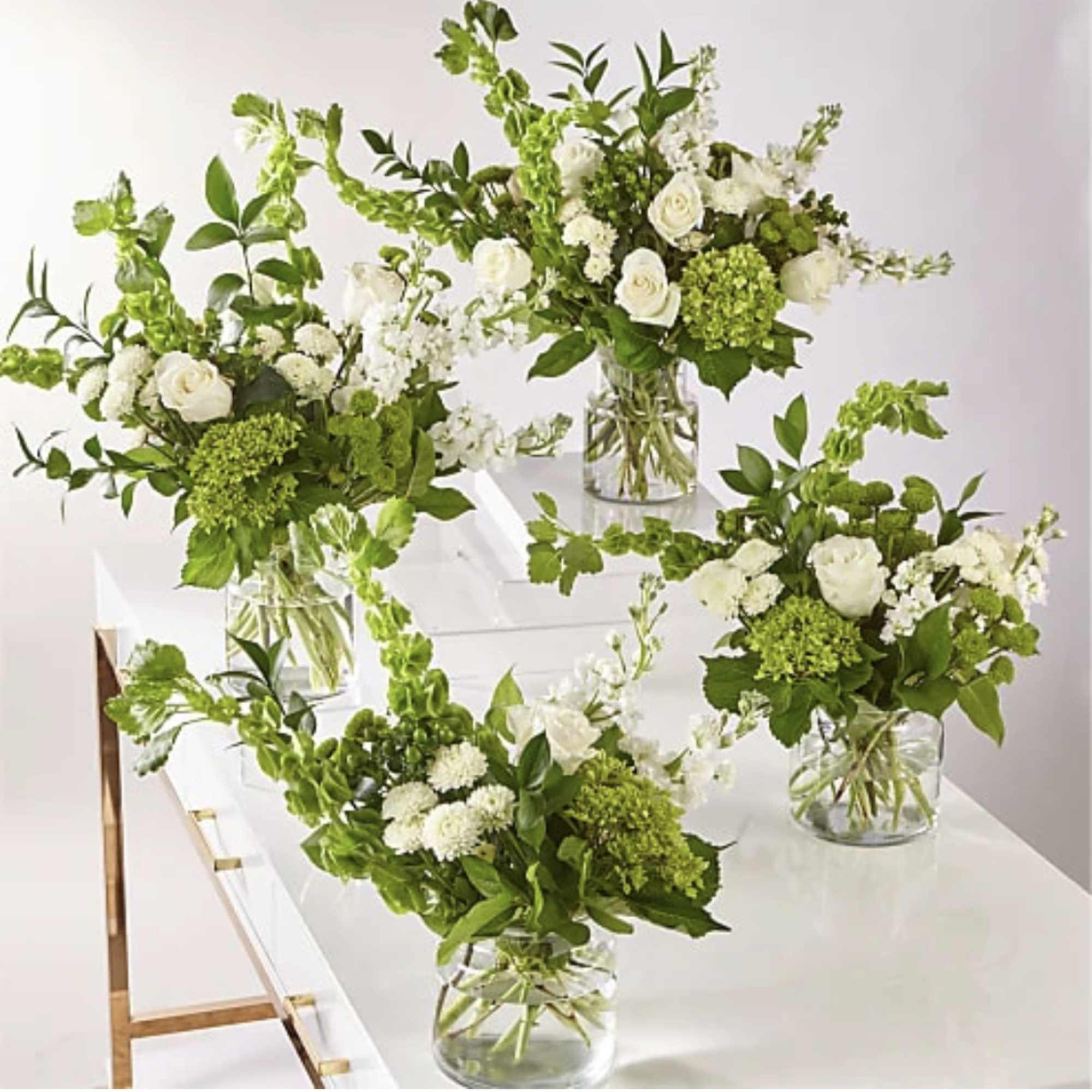 Four white and green floral arrangements in clear glass vases on a white table