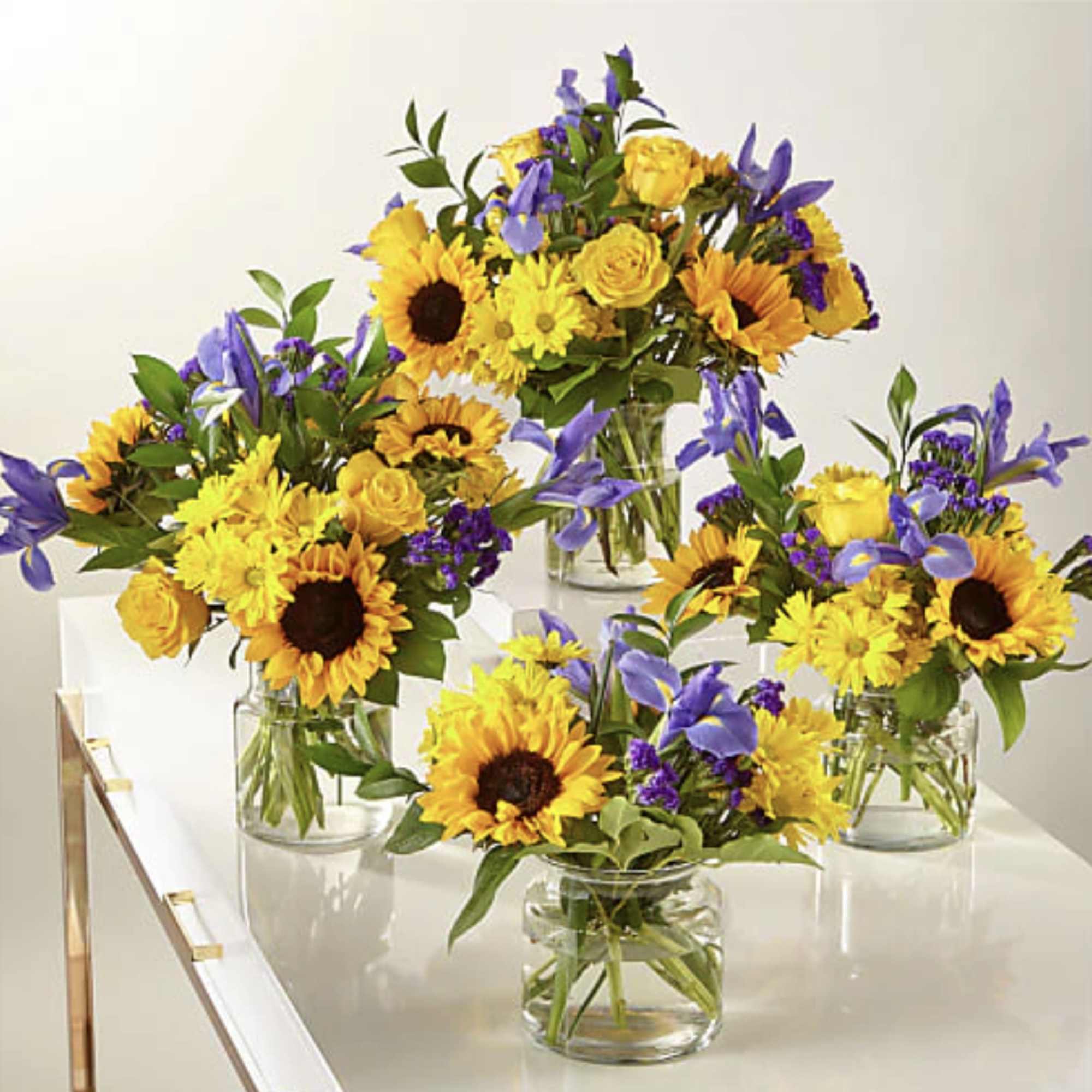 Five mixed bouquets of sunflowers and purple flowers in clear glass vases
