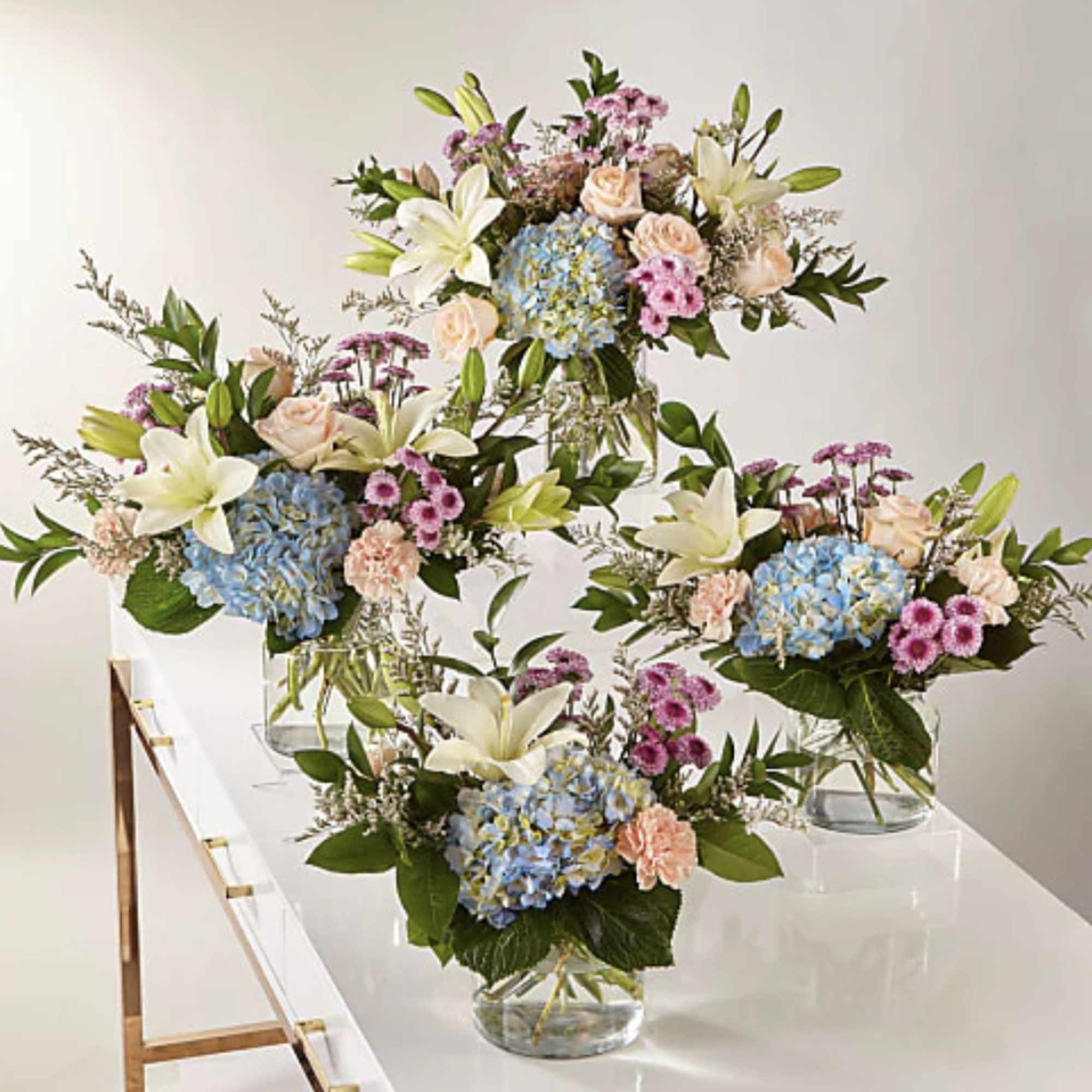 Four mixed floral arrangements in clear glass vases on a white table