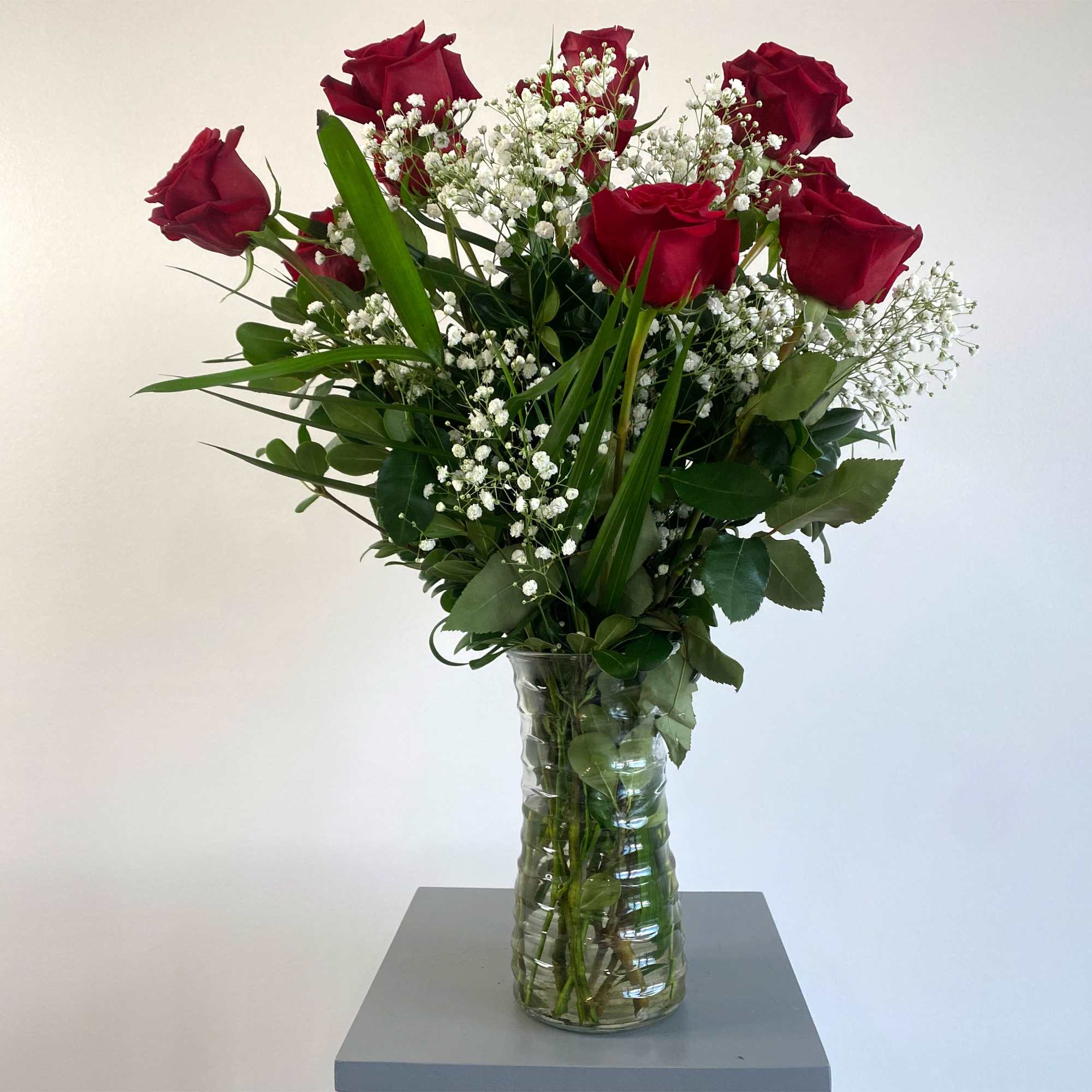 Red roses arranged in a clear glass vase with baby's breath