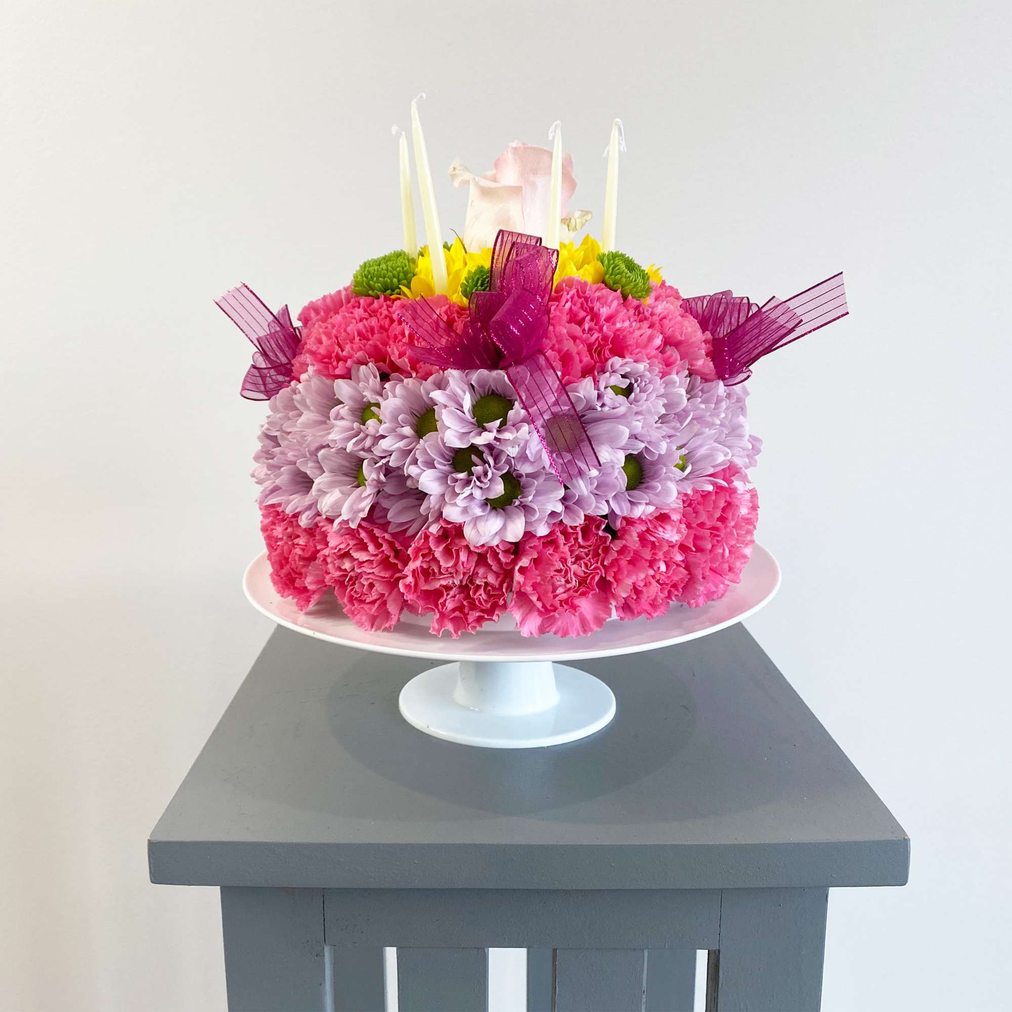Pink and lavender flower cake with candles on a white pedestal stand