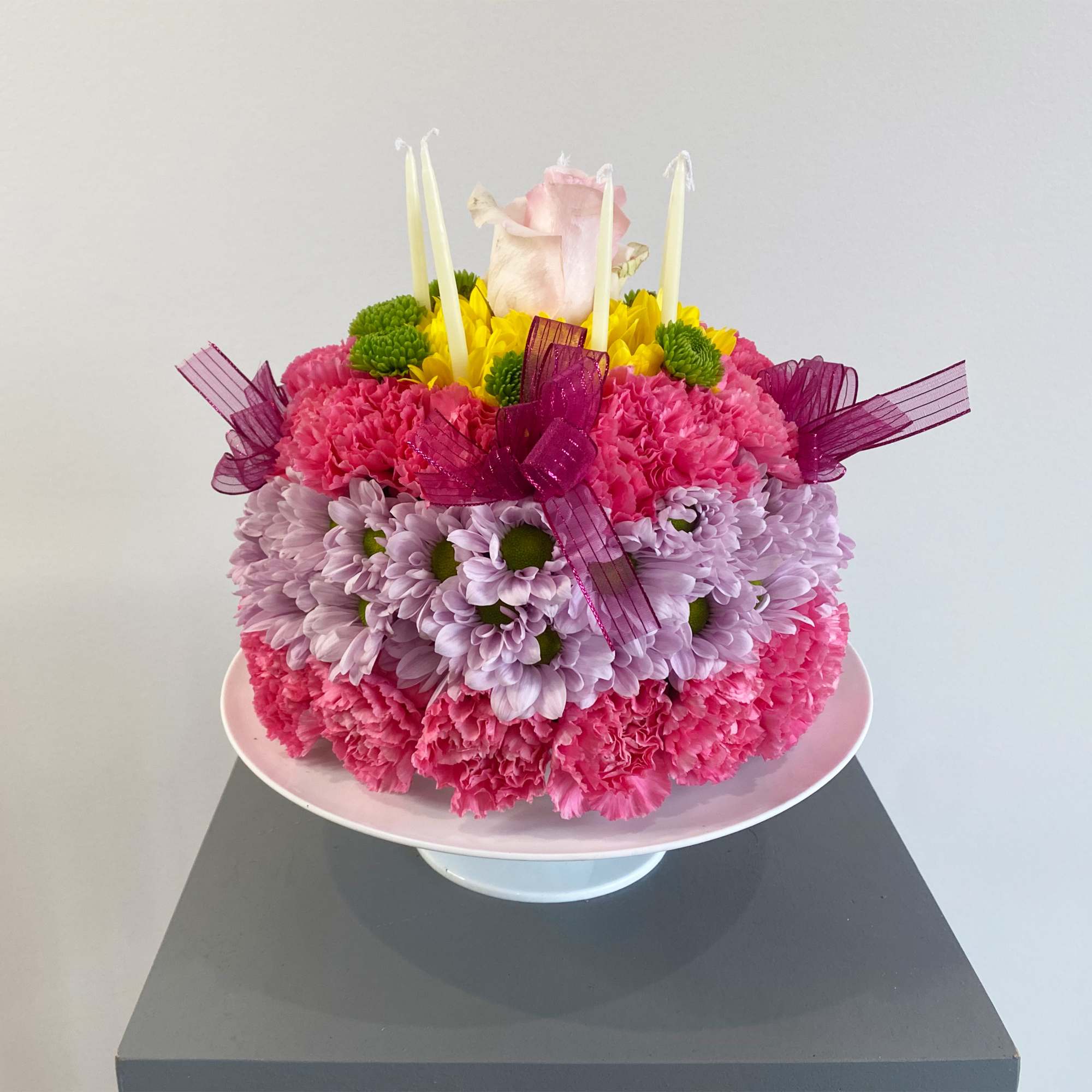 Round floral cake with pink, lavender, and yellow flowers on a pedestal