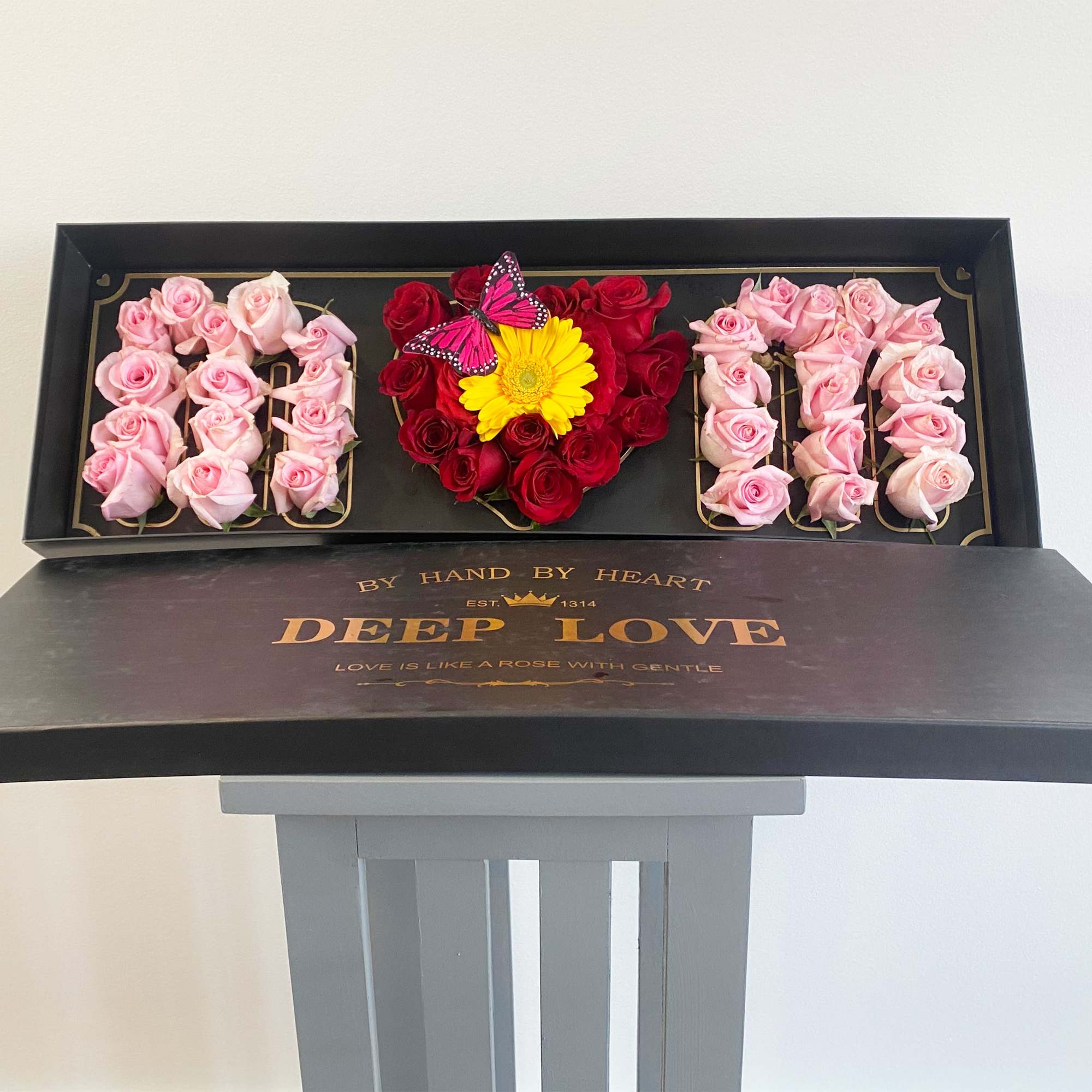 Heart-shaped rose arrangement in a black gift box with a yellow flower and butterfly