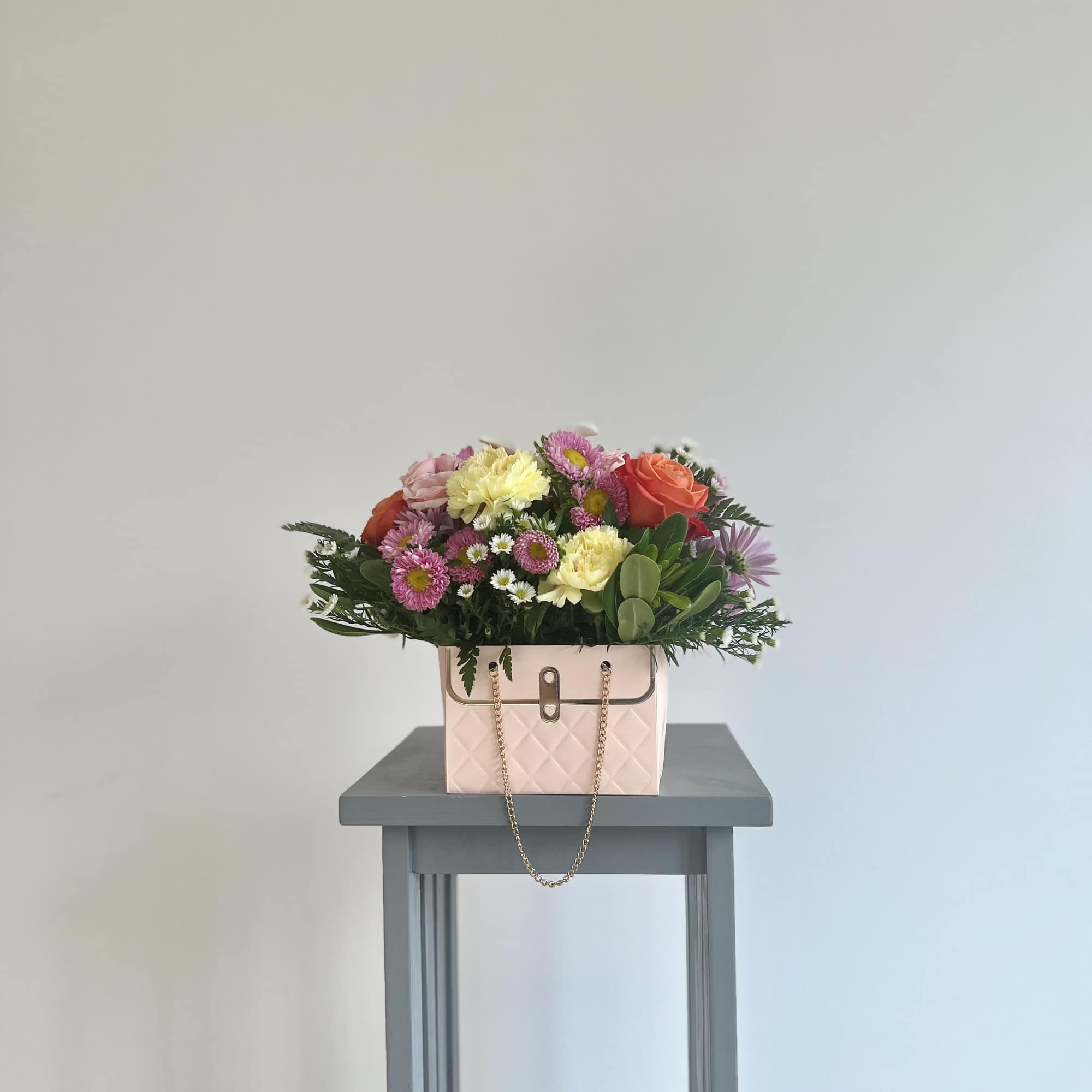 Mixed bouquet in a pink handbag-style container on a small table