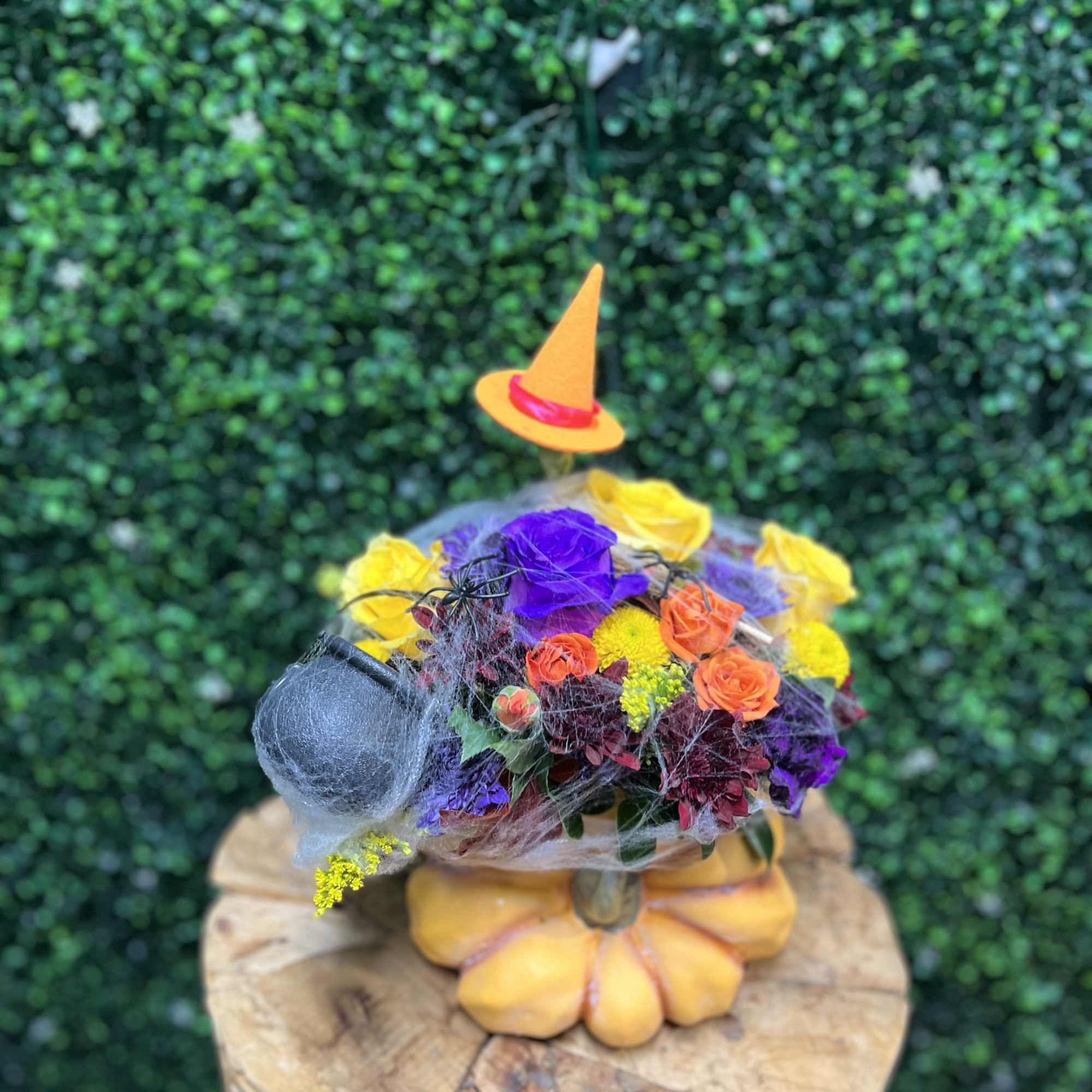 Colorful floral arrangement in a pumpkin-shaped container with a small witch hat