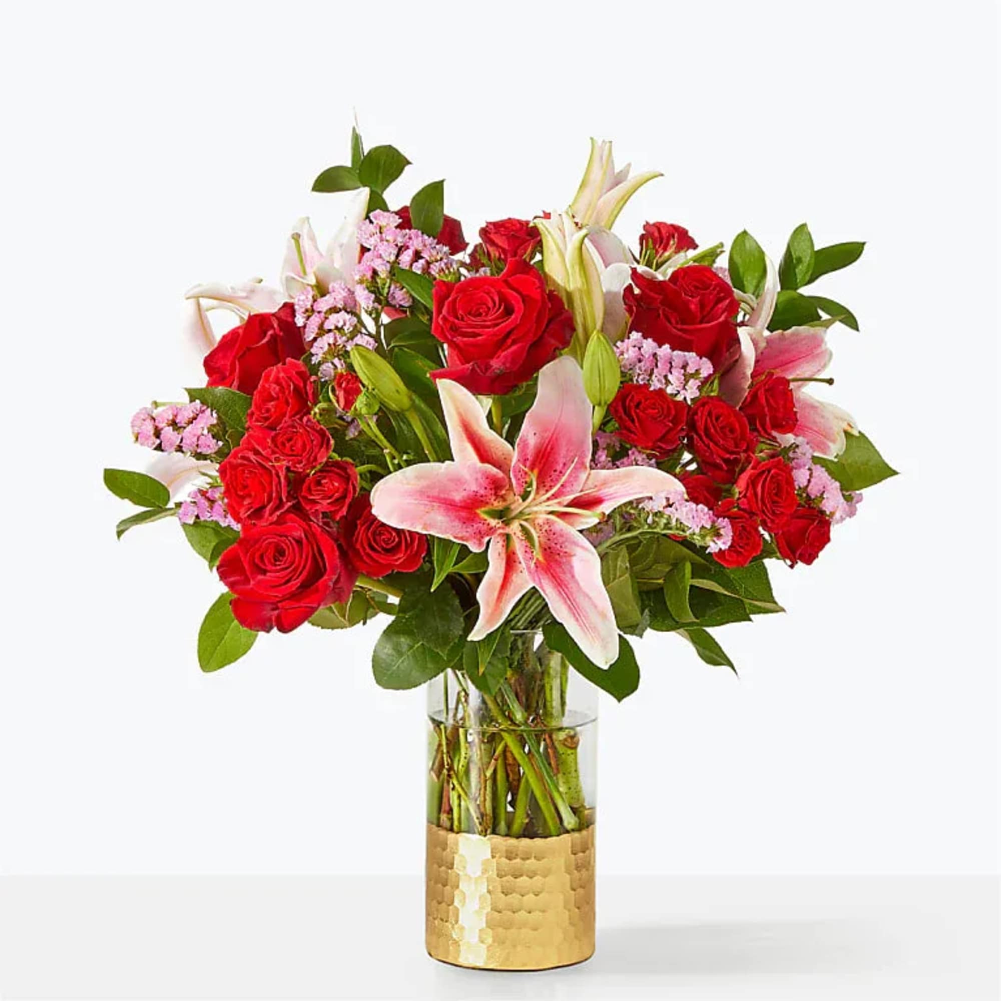Red roses and pink lilies in a clear vase with a gold base