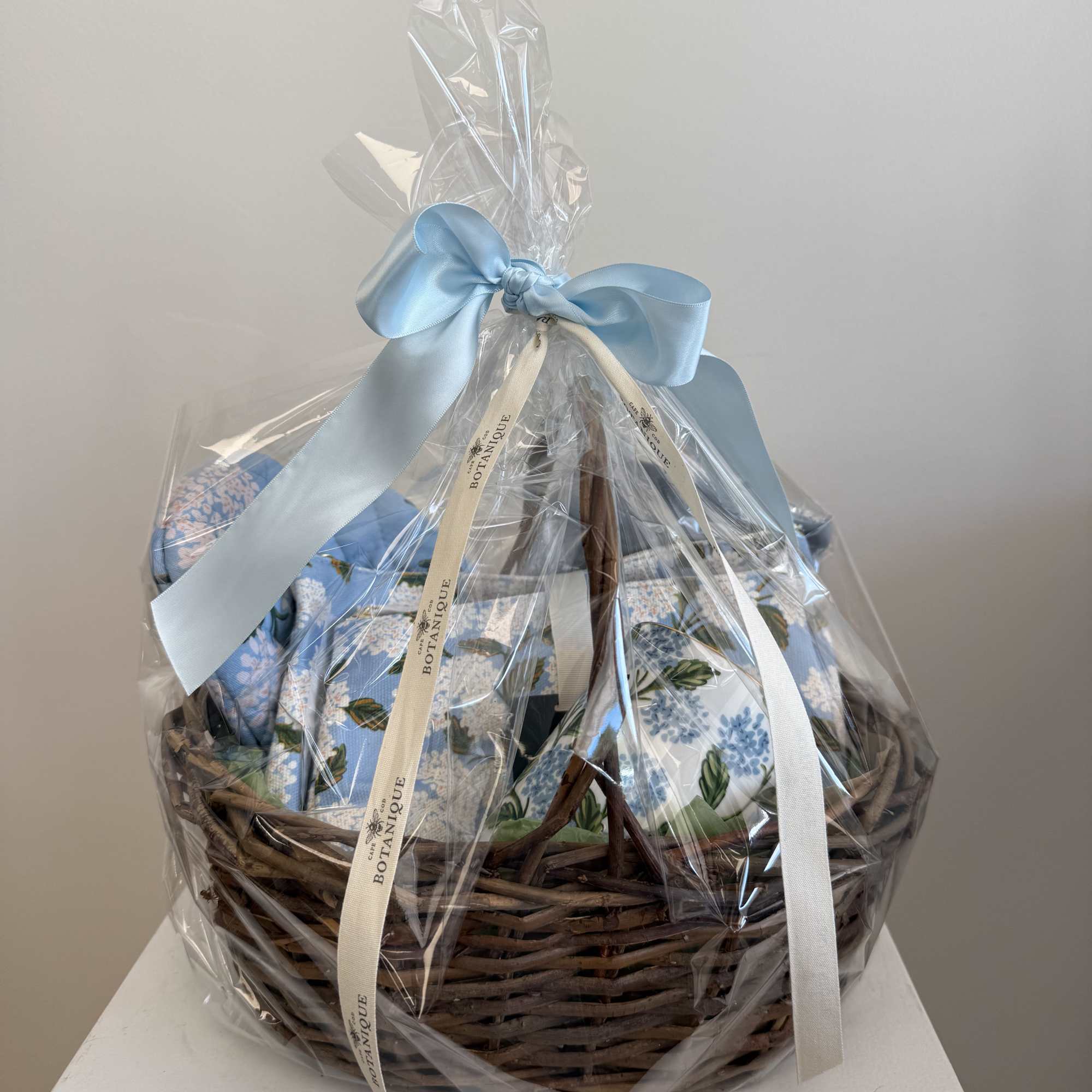 Gift basket wrapped in clear cellophane with a blue ribbon