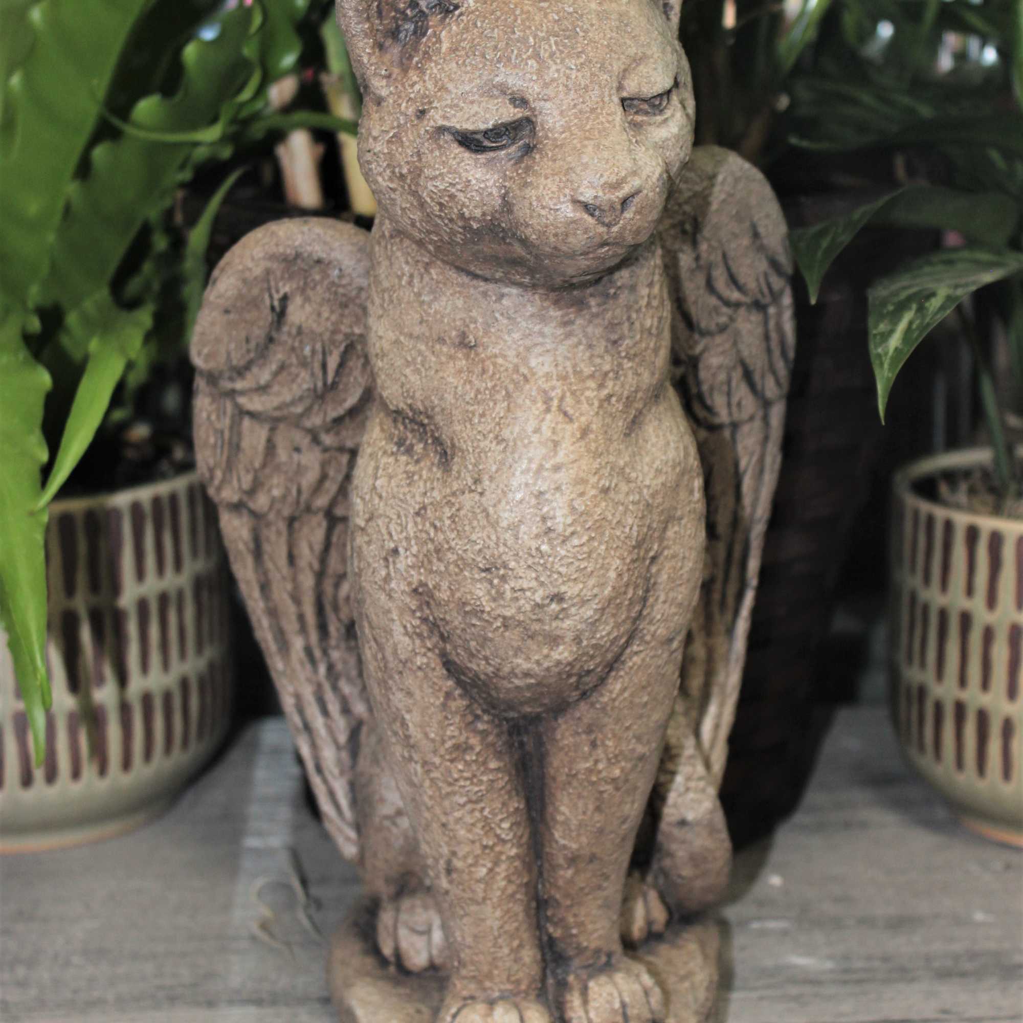 Stone cat statue with wings among potted plants