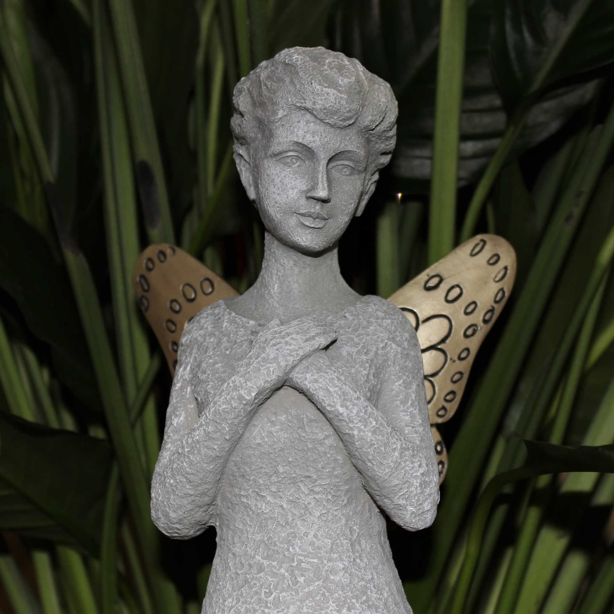 Gray angel figurine with patterned wings against dark green foliage