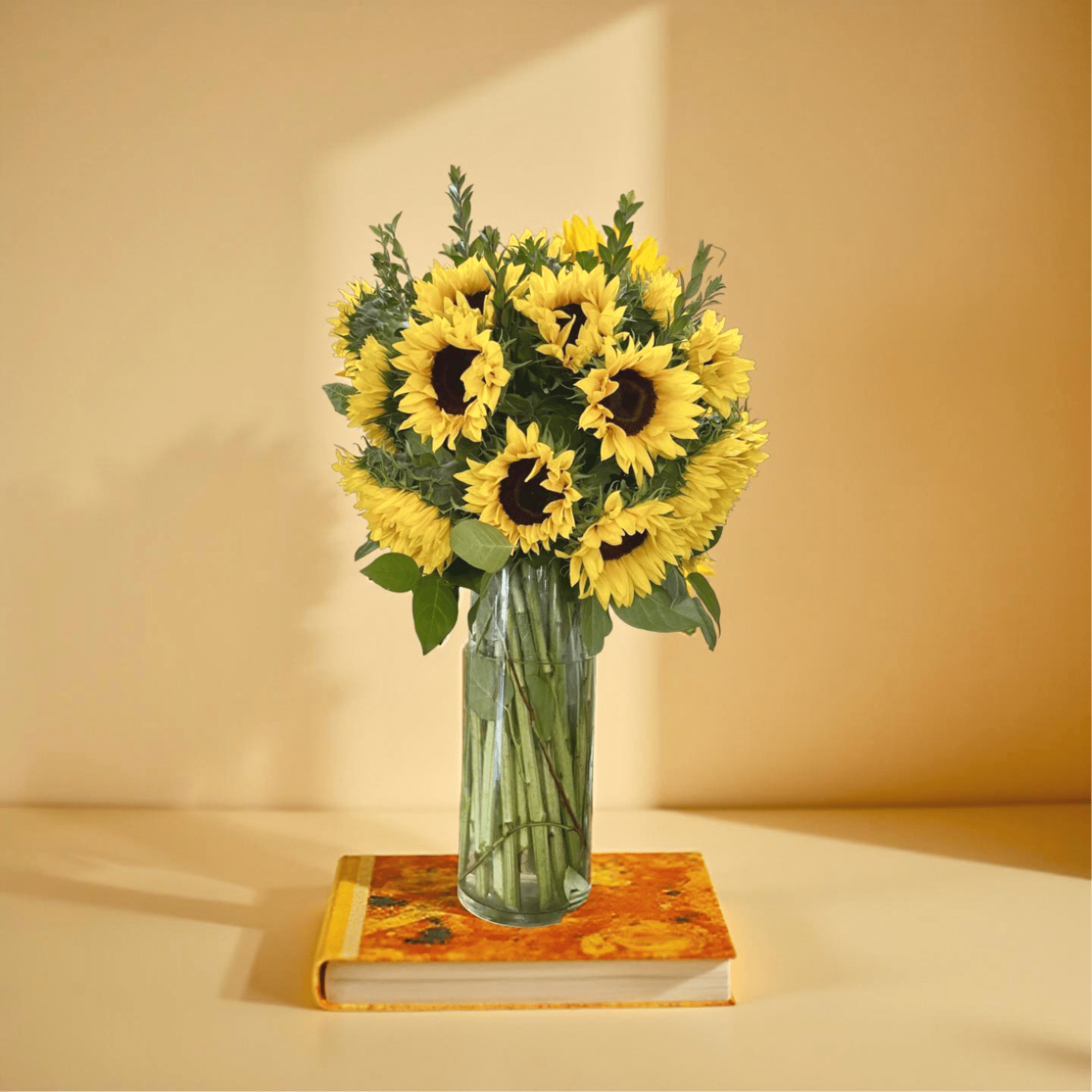 Tall bouquet of bright yellow sunflowers in a clear glass vase set on a colorful book.