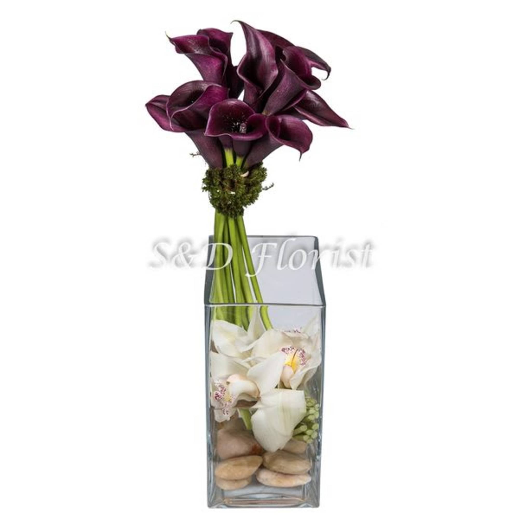 Purple calla lilies in a tall glass vase with white flowers and stones
