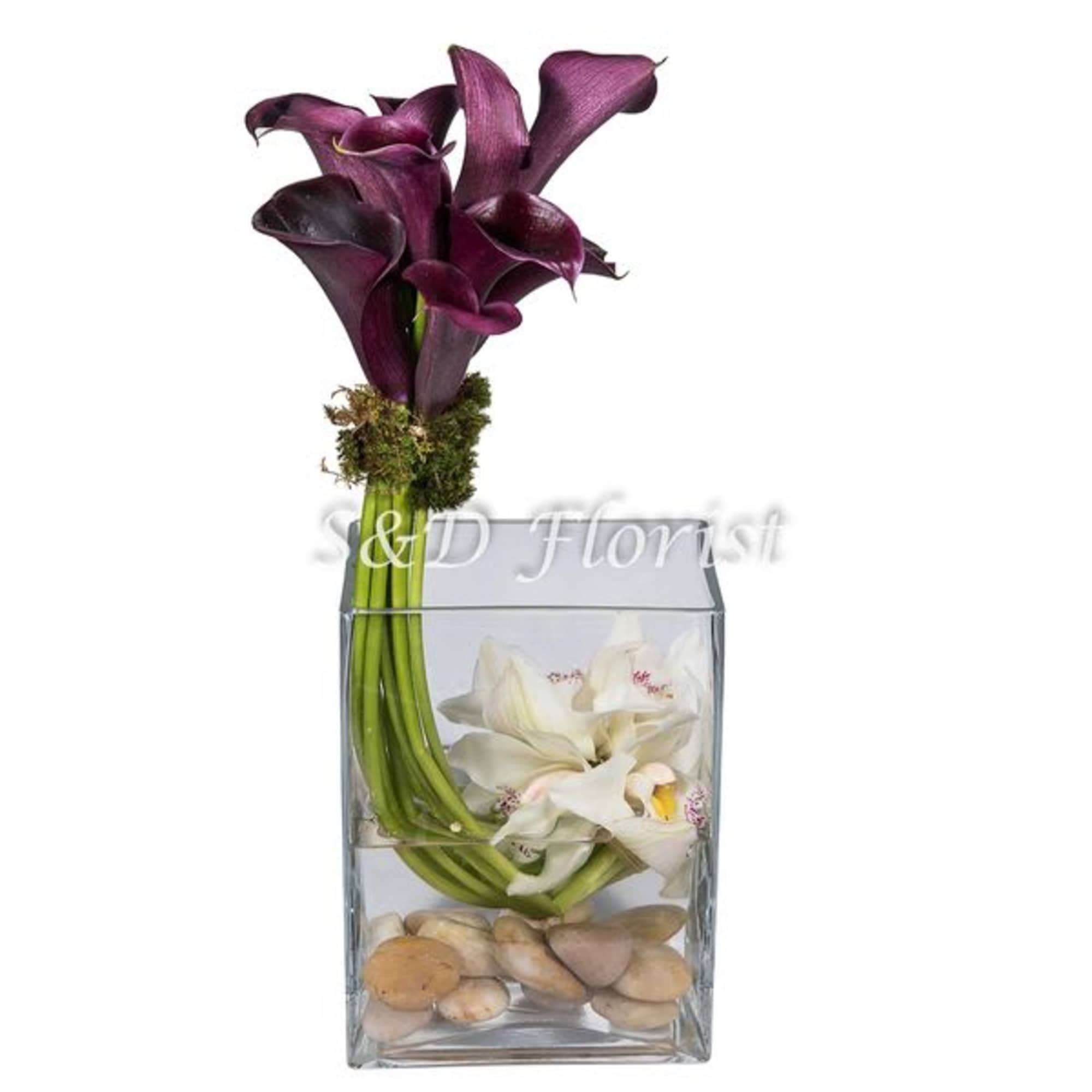 Purple and white calla lilies in a clear glass vase with stones