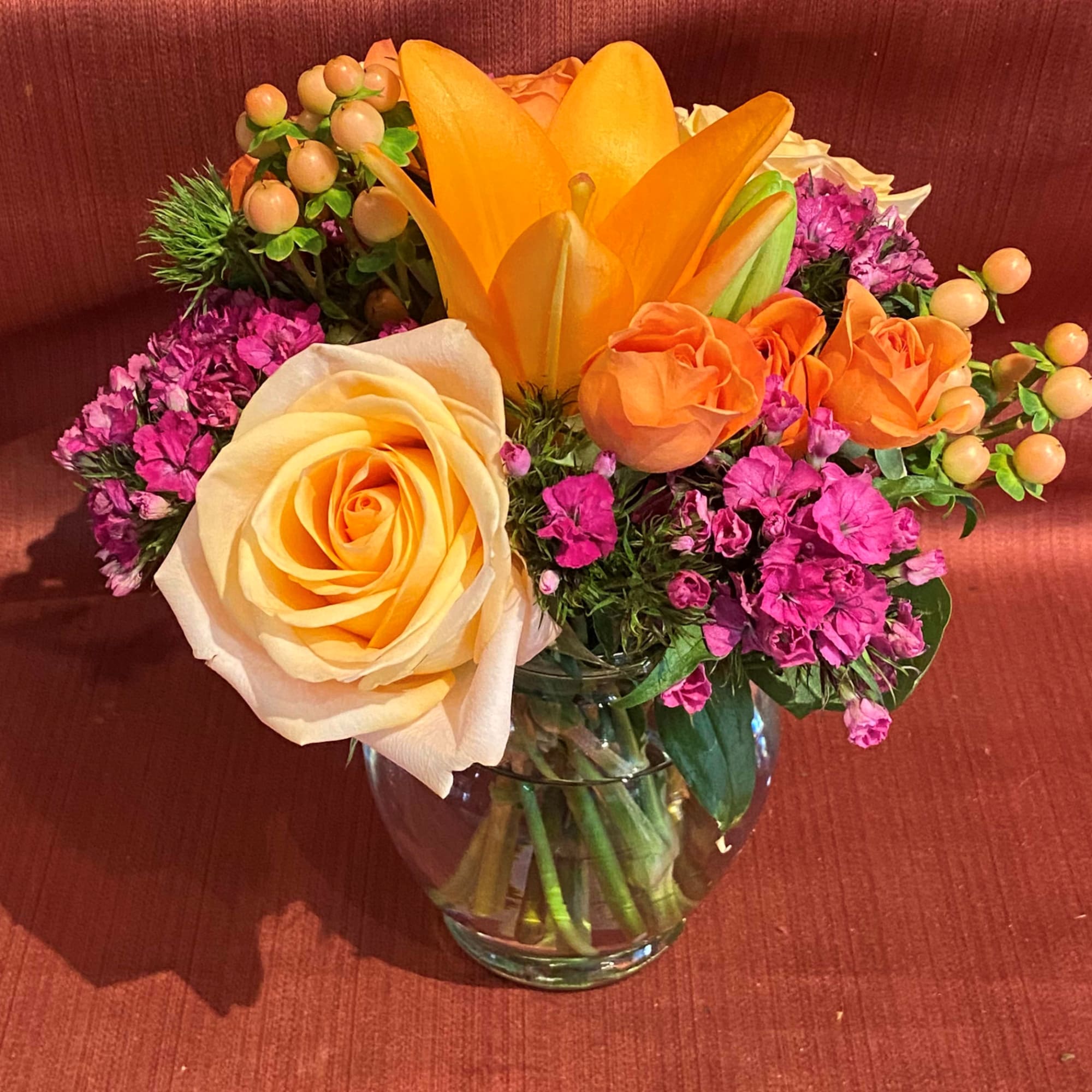 Orange and cream roses with a lily in a glass vase