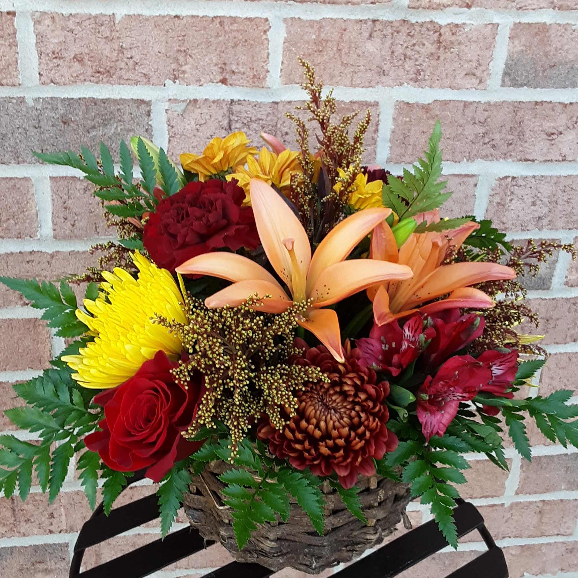 Mixed bouquet in a woven basket with red, yellow, and peach flowers
