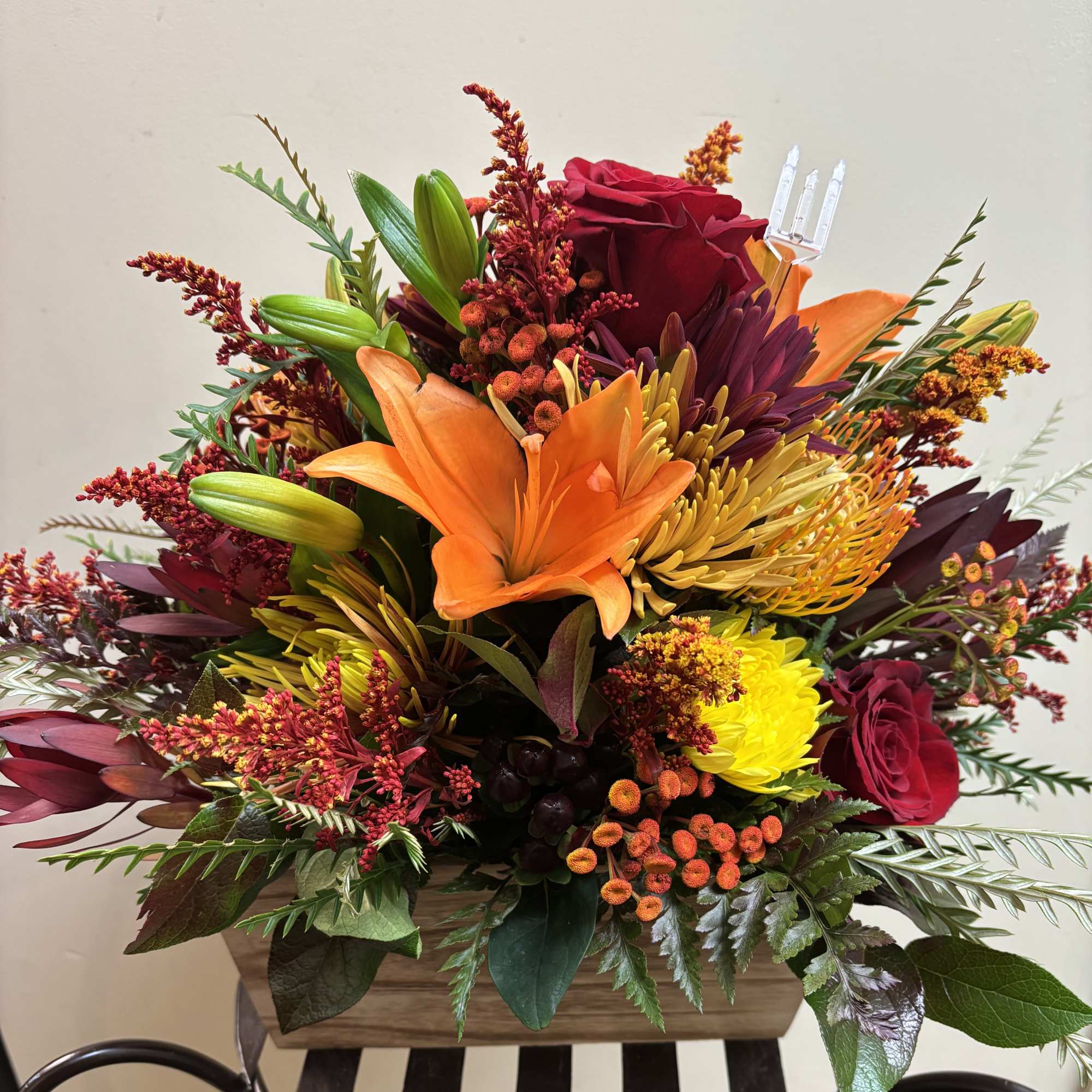 Mixed bouquet with orange lilies, red roses, and yellow chrysanthemums in a wooden container