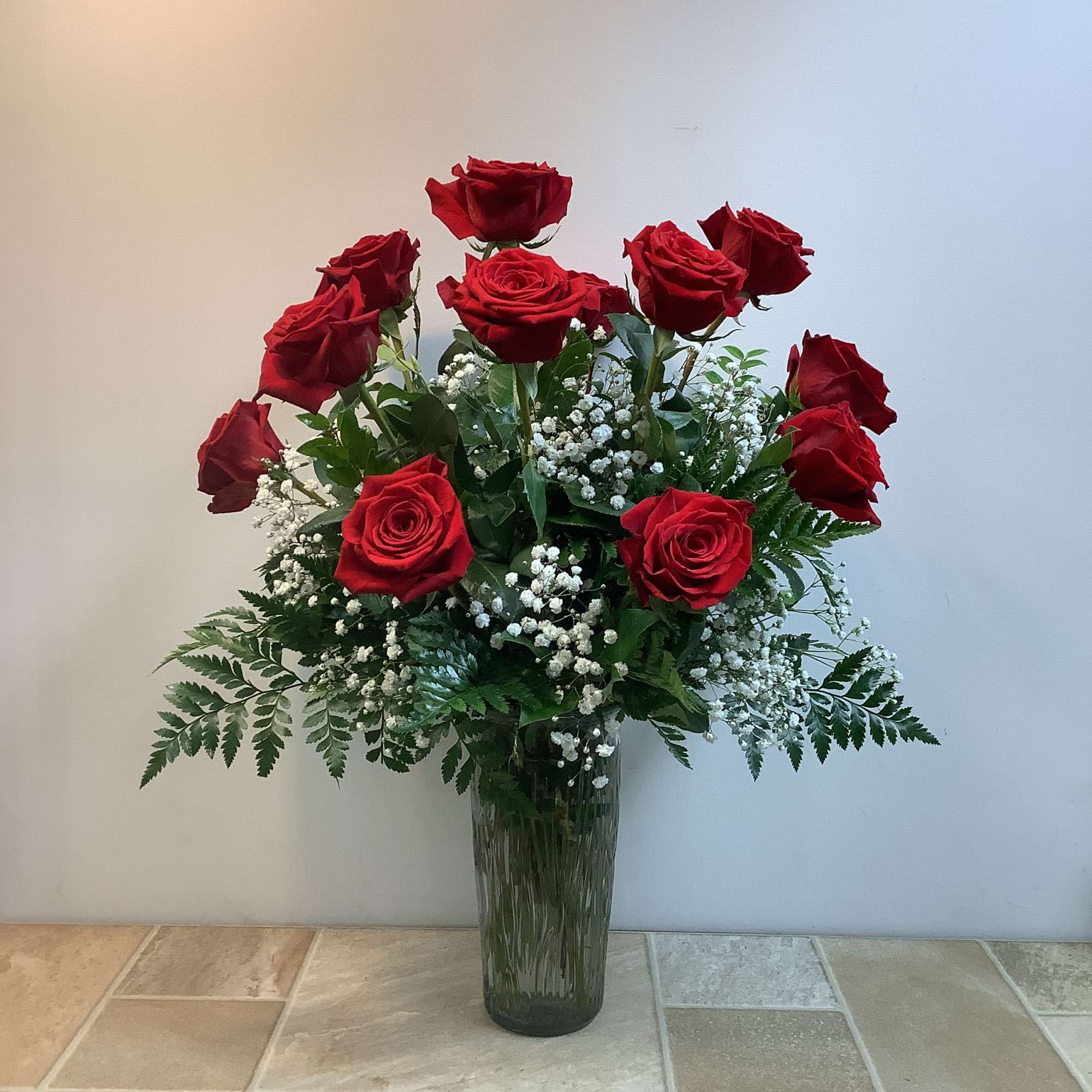 Red roses arranged in a tall glass vase with white baby's breath
