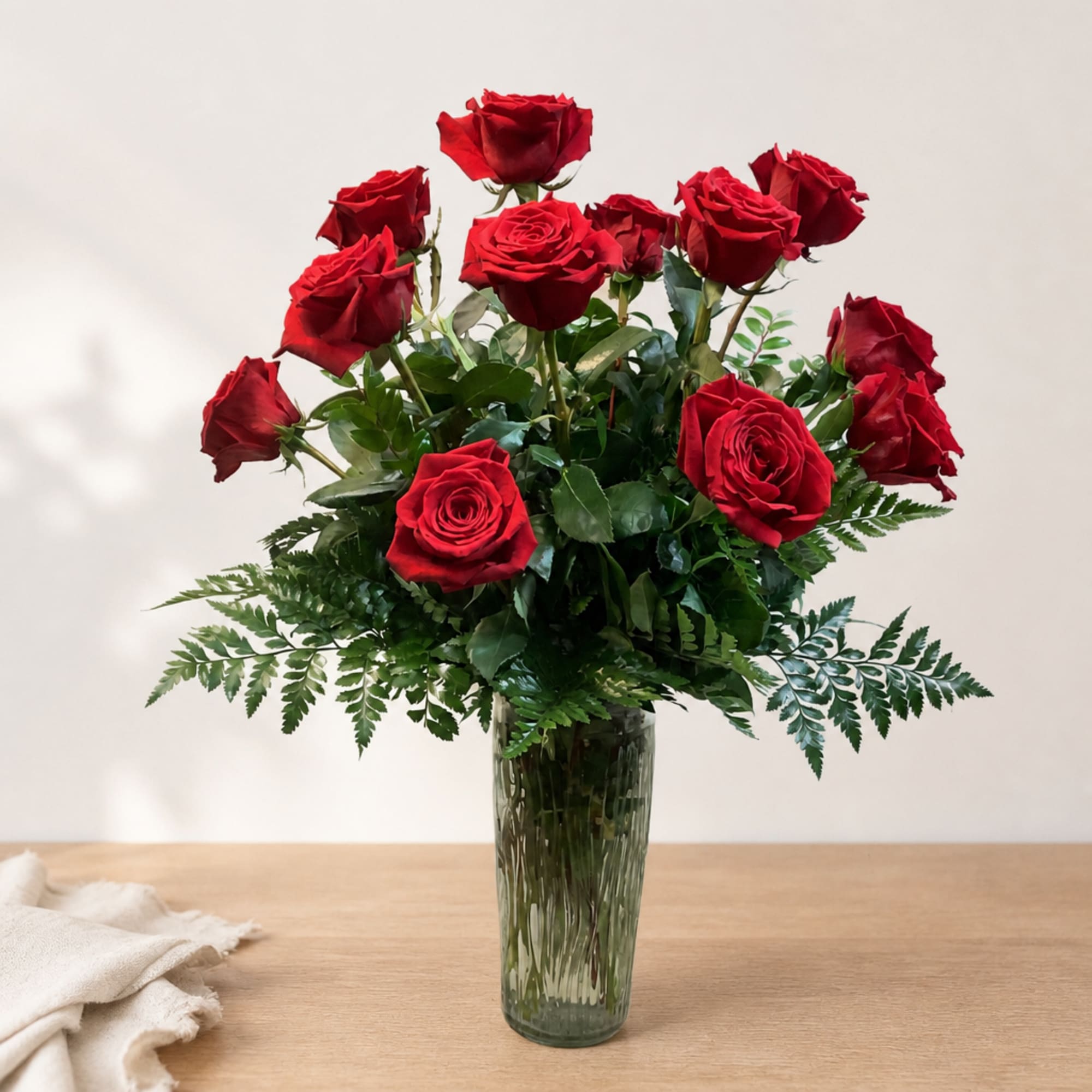 Red roses arranged in a clear glass vase with greenery