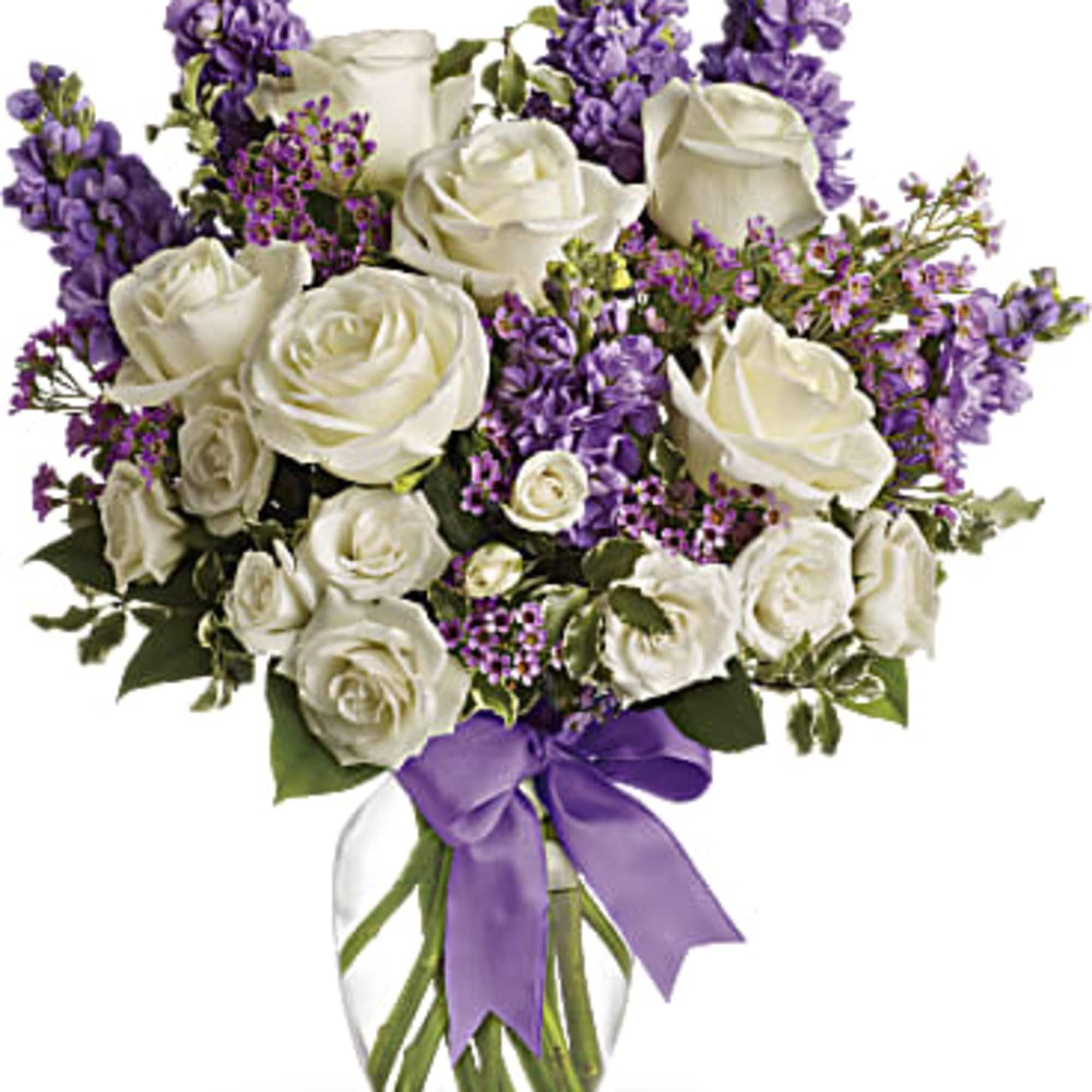 White roses and purple flowers in a clear glass vase with a purple ribbon
