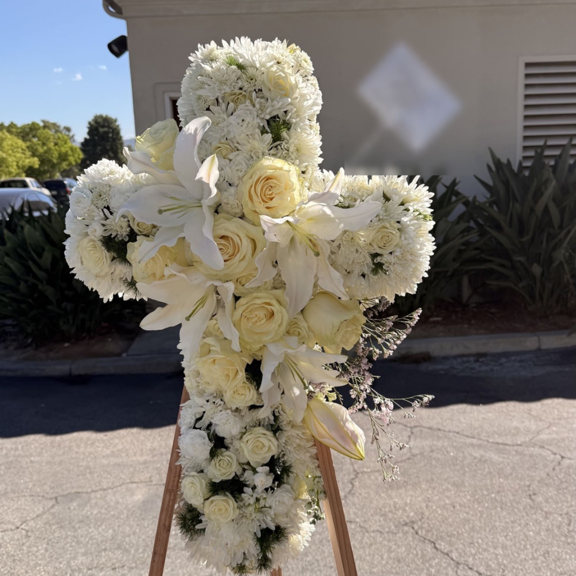 White floral cross arrangement with roses and lilies on a wooden easel