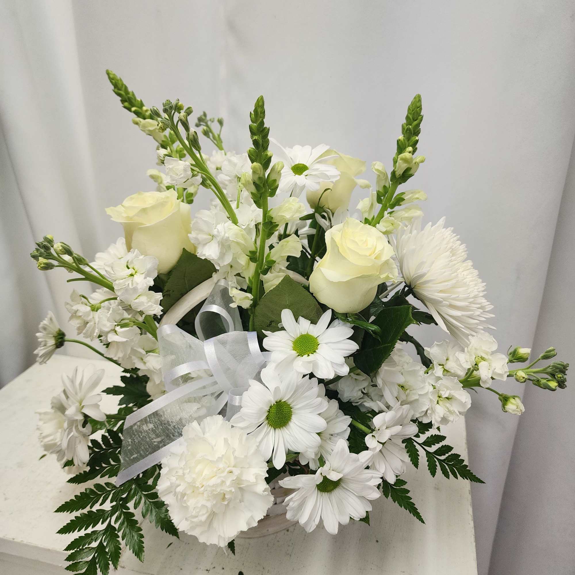 White floral arrangement with roses, daisies, and ribbon in a vase