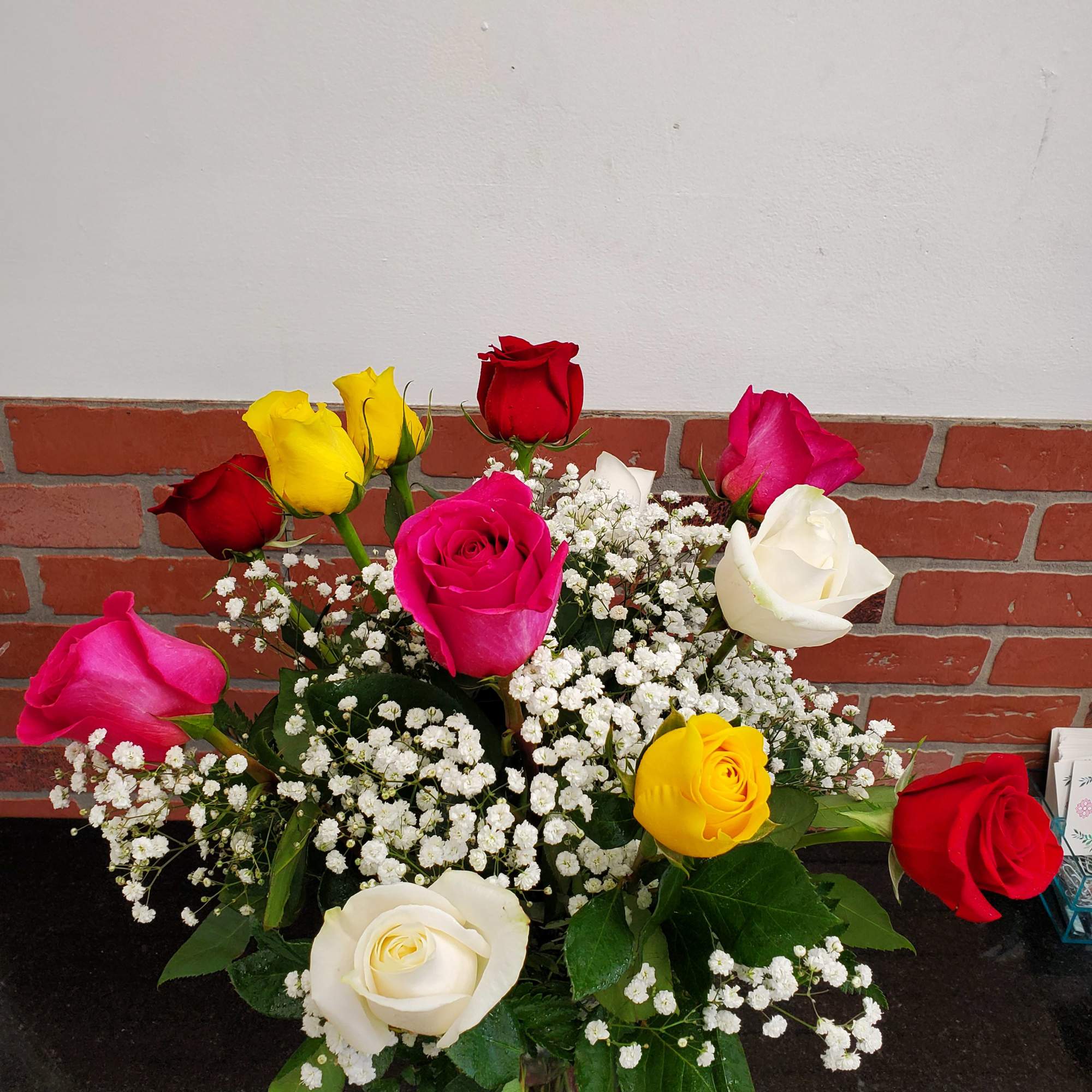 Mixed red, pink, yellow, and white roses with baby's breath in a clear glass vase on a dark countertop