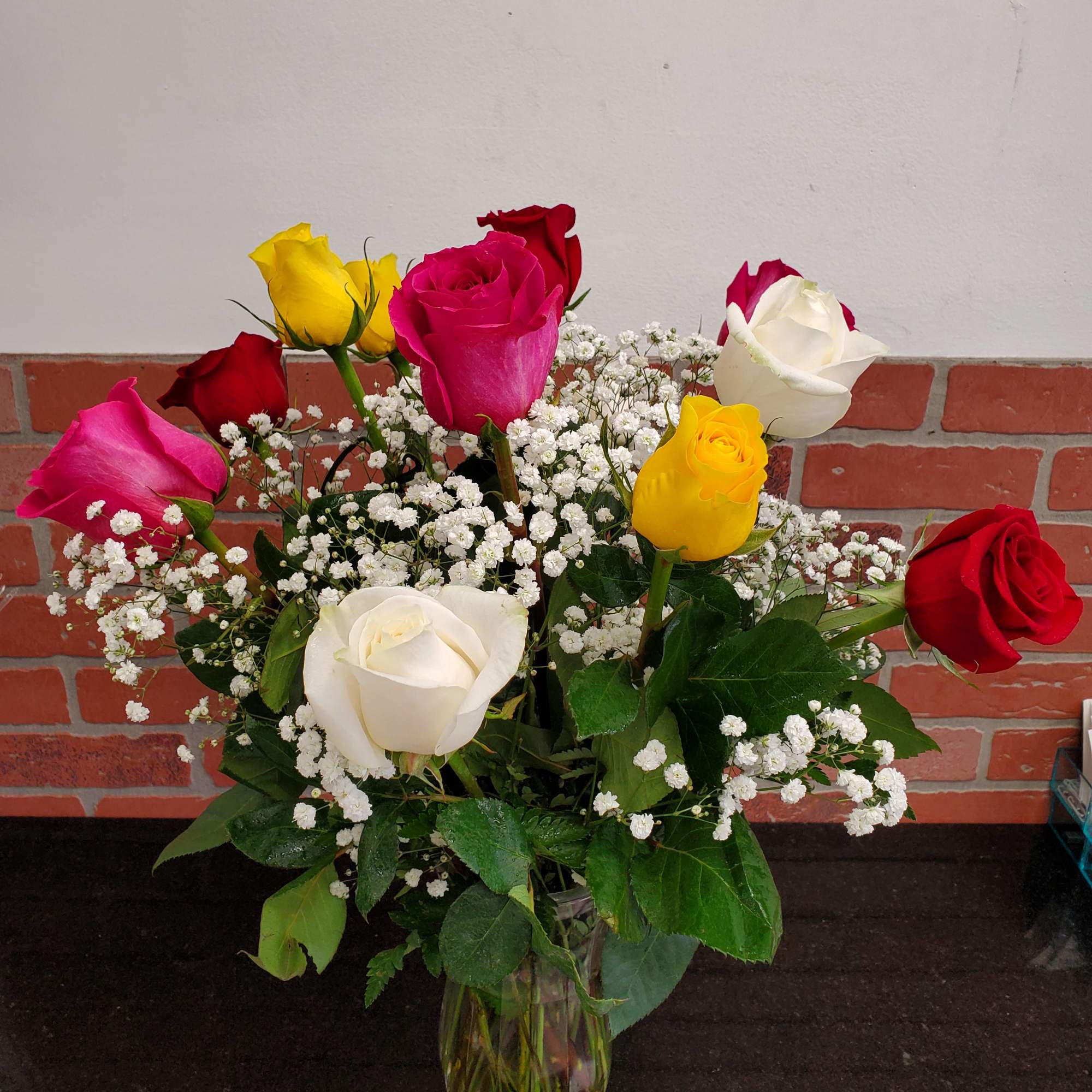 Mixed red, pink, yellow, and white roses with baby's breath in a clear glass vase
