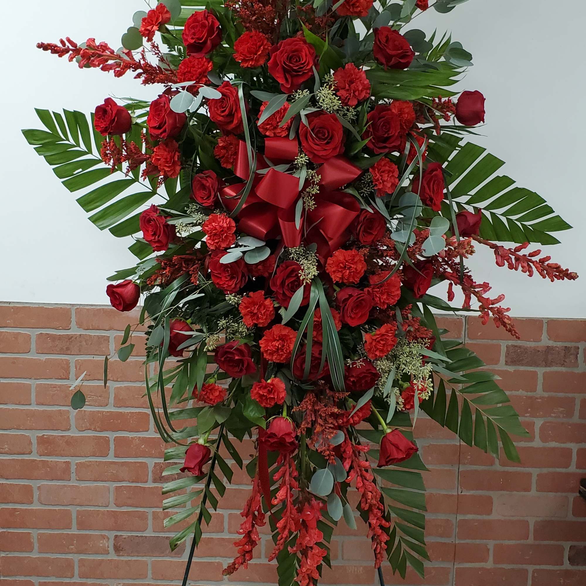 Tall red rose and carnation standing spray with palm leaves on a metal easel