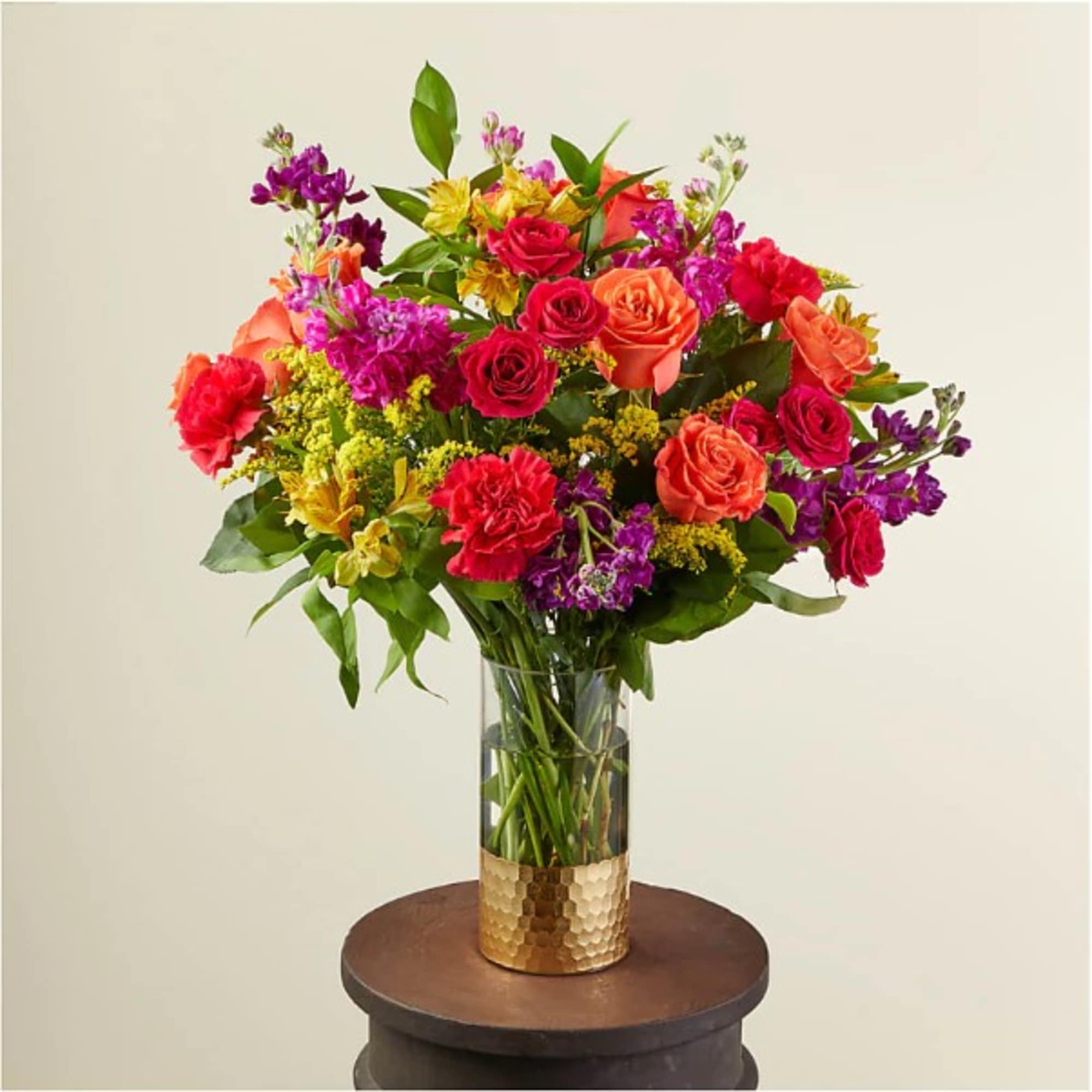 Tall arrangement of bright pink, orange, yellow, and purple flowers in a glass vase with a gold base