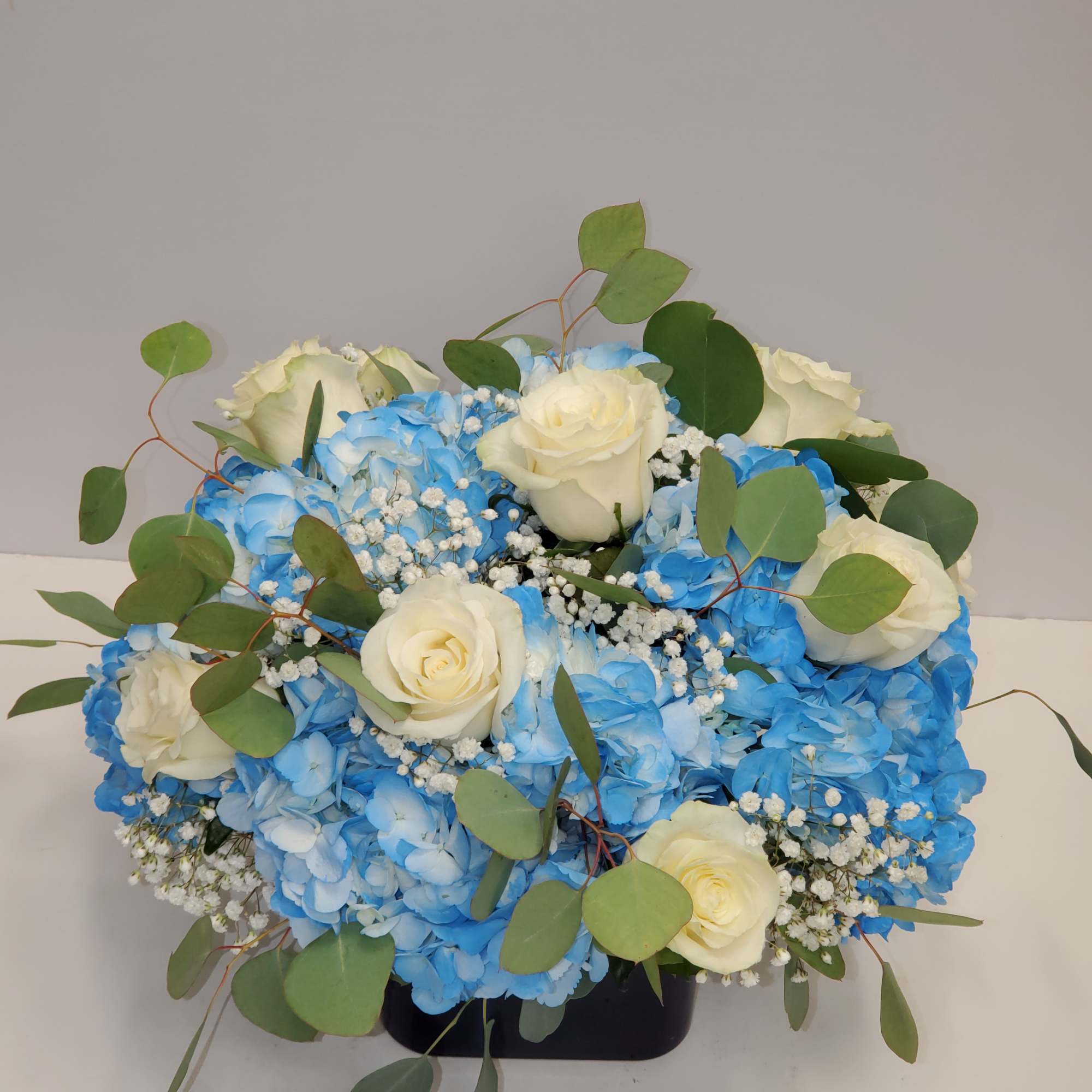 Low arrangement of blue hydrangeas and white roses with baby's breath in a black cube vase