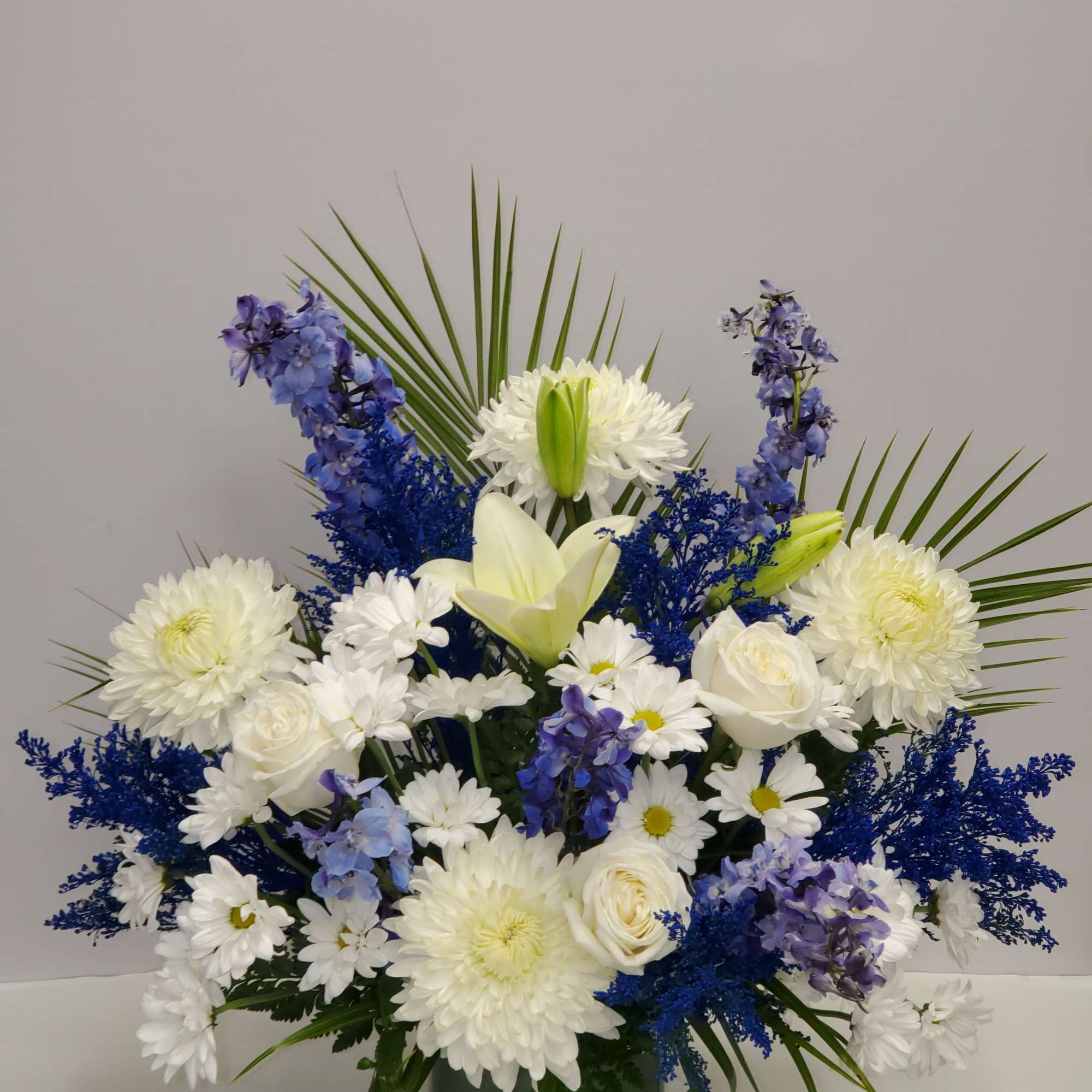 Tall white and blue flower arrangement with palm fronds in a green square vase