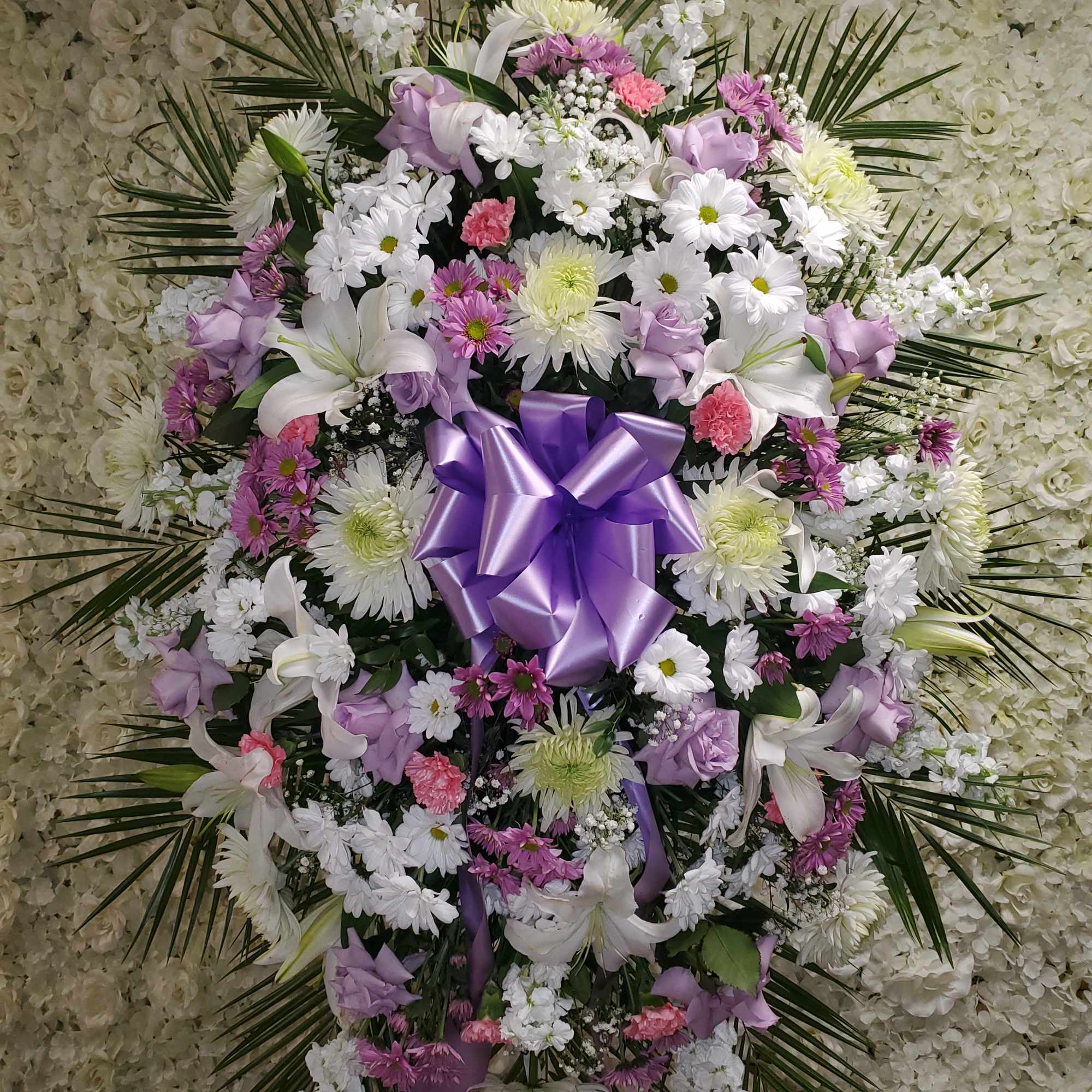 Tall standing spray of white, pink, and lavender flowers with a large lavender bow