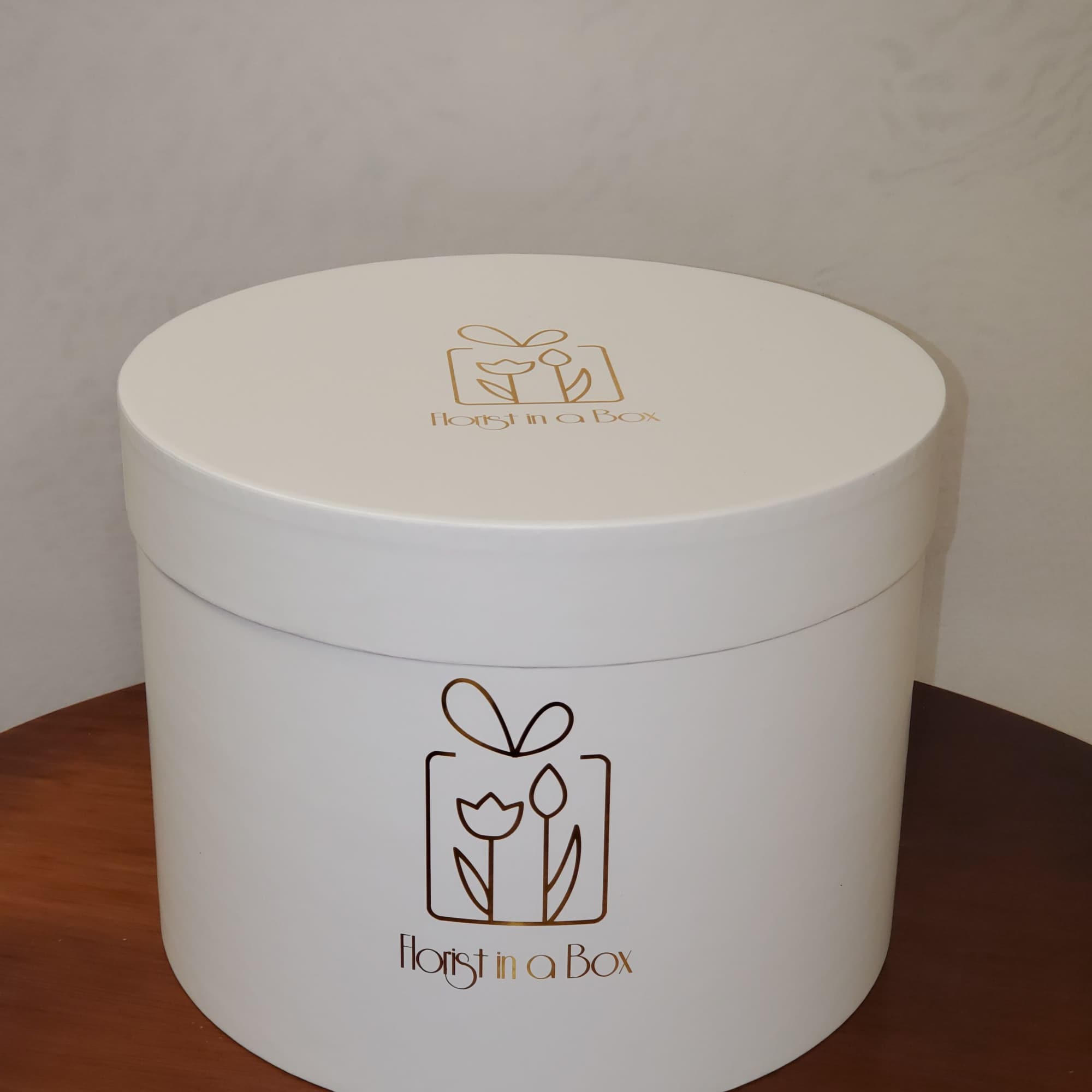 Large round white hat box with gold Florist in a Box logo on a wooden table