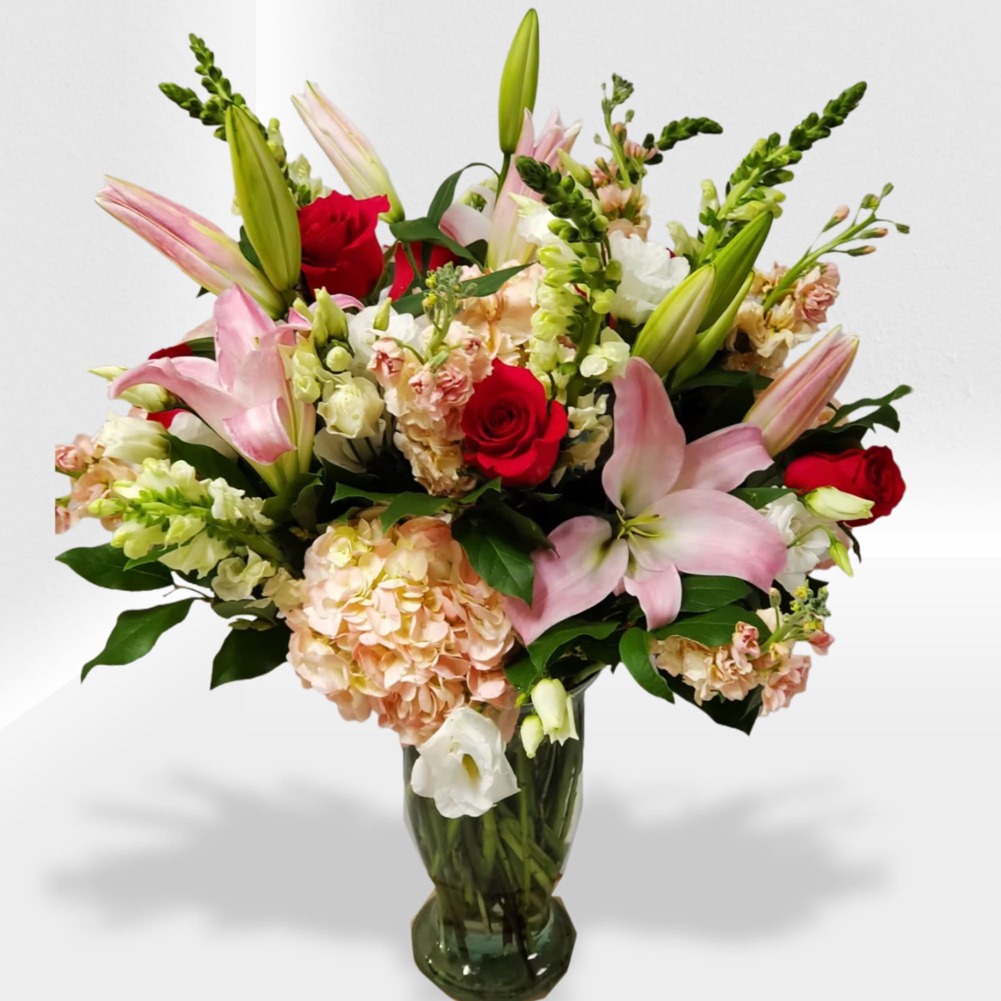 Tall mixed arrangement of pink lilies, red roses, and peach hydrangeas in a glass vase